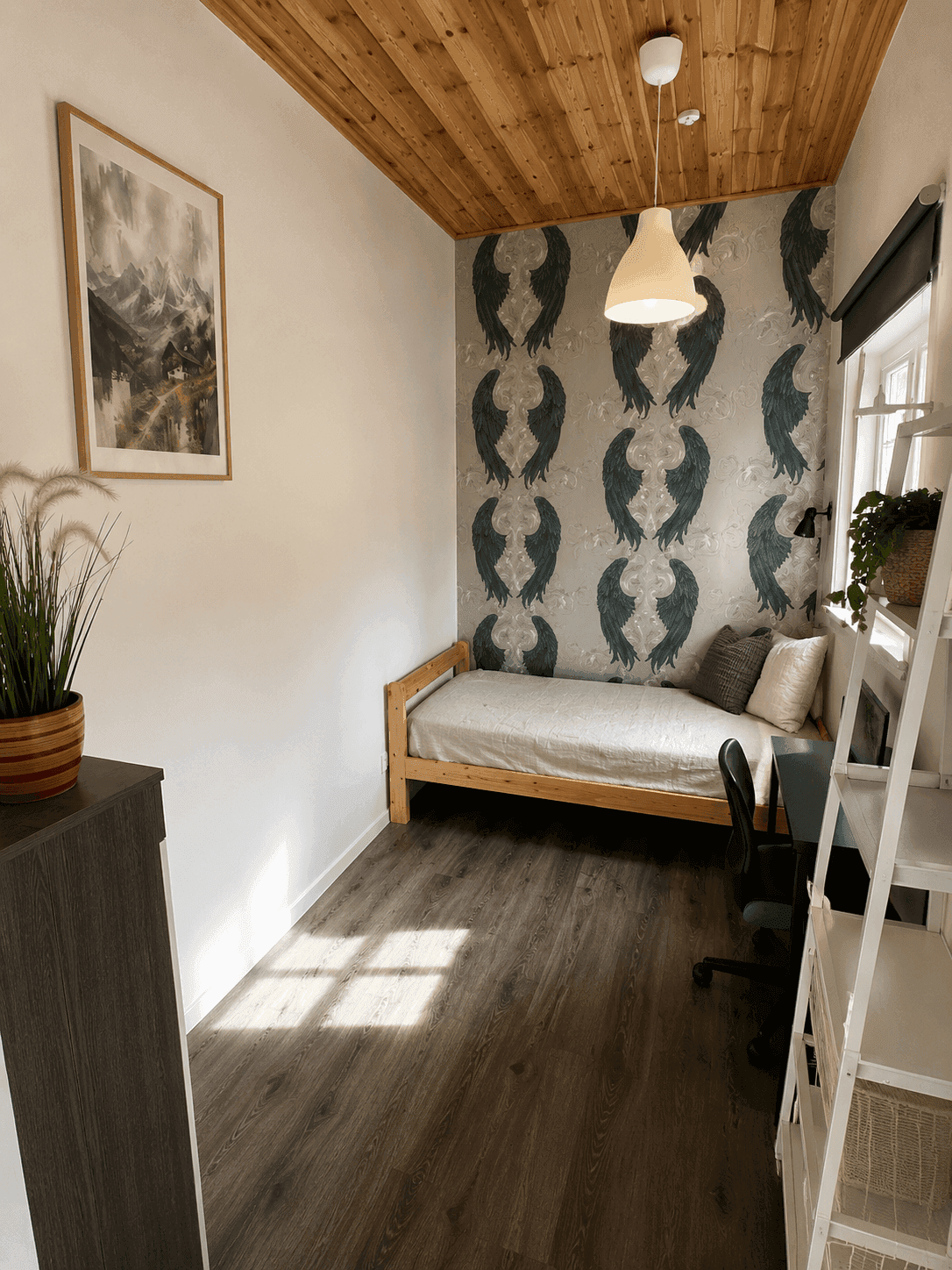 Kleines Arbeitszimmer mit Einzelbett, Schreibtisch und gemusterter Tapetenwand.