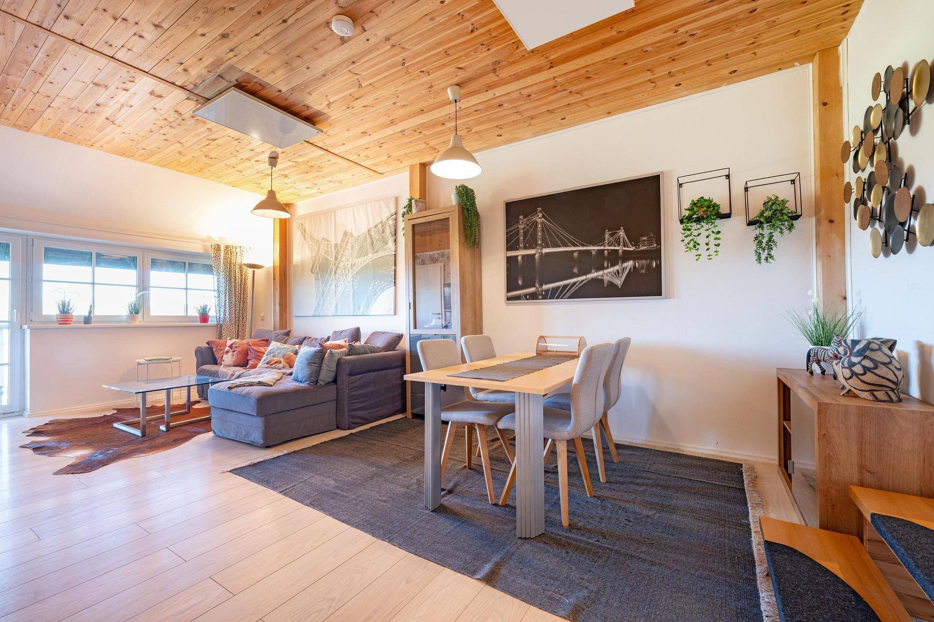 Geräumiger Wohn- und Essbereich mit Holzbalkendecke, bequemer Couch und viel Tageslicht.
