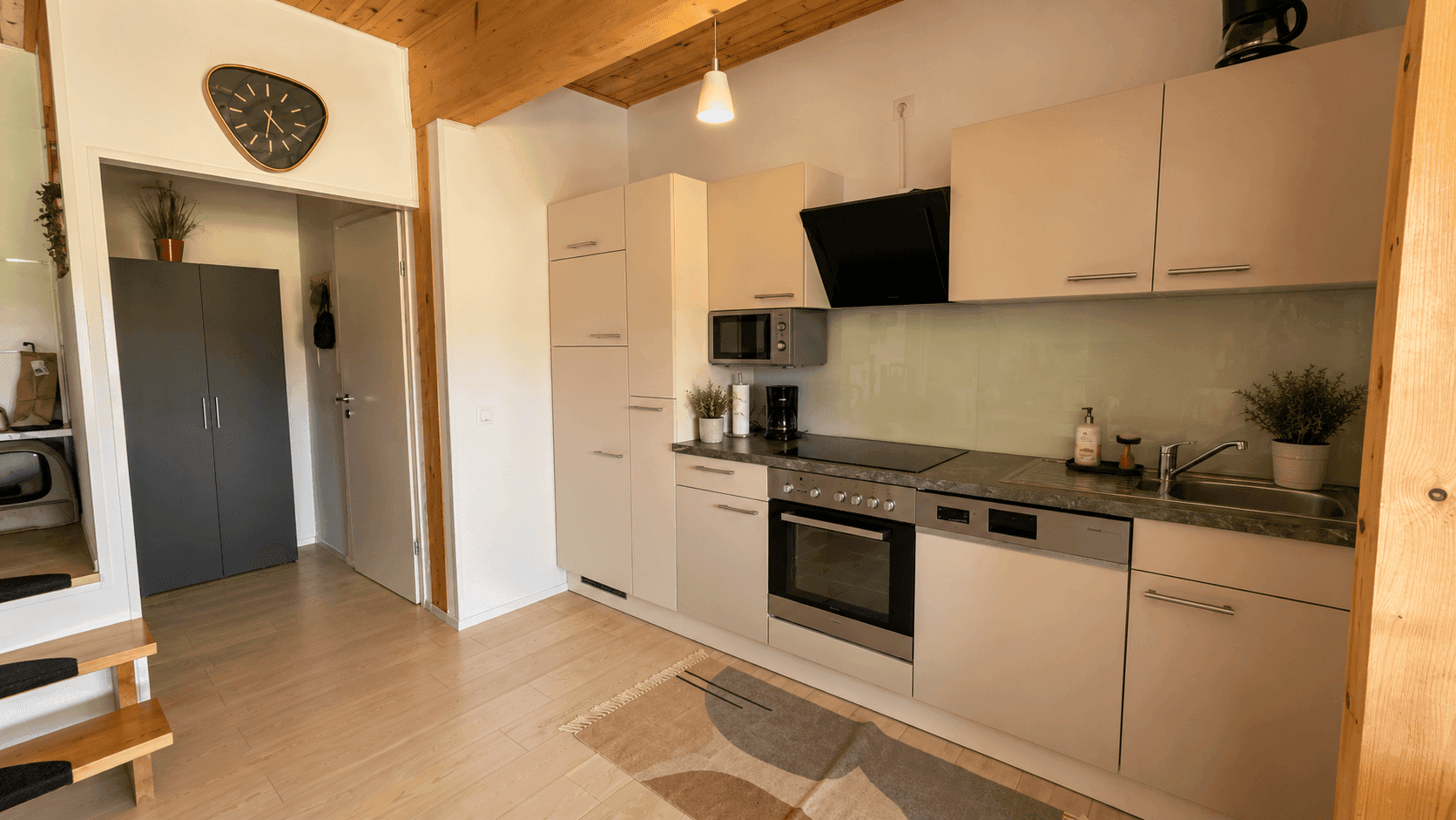 Moderne Einbauküche mit weißen Schränken, dunkler Arbeitsplatte und Holzbalkendecke.