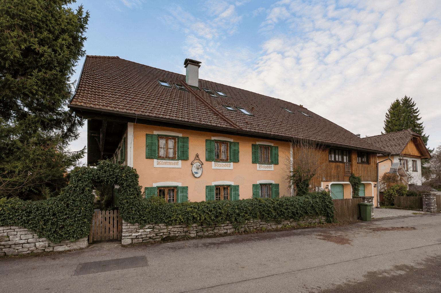 Traditionelles Haus mit oranger Fassade, grünen Fensterläden und gepflegtem Vorgarten.
