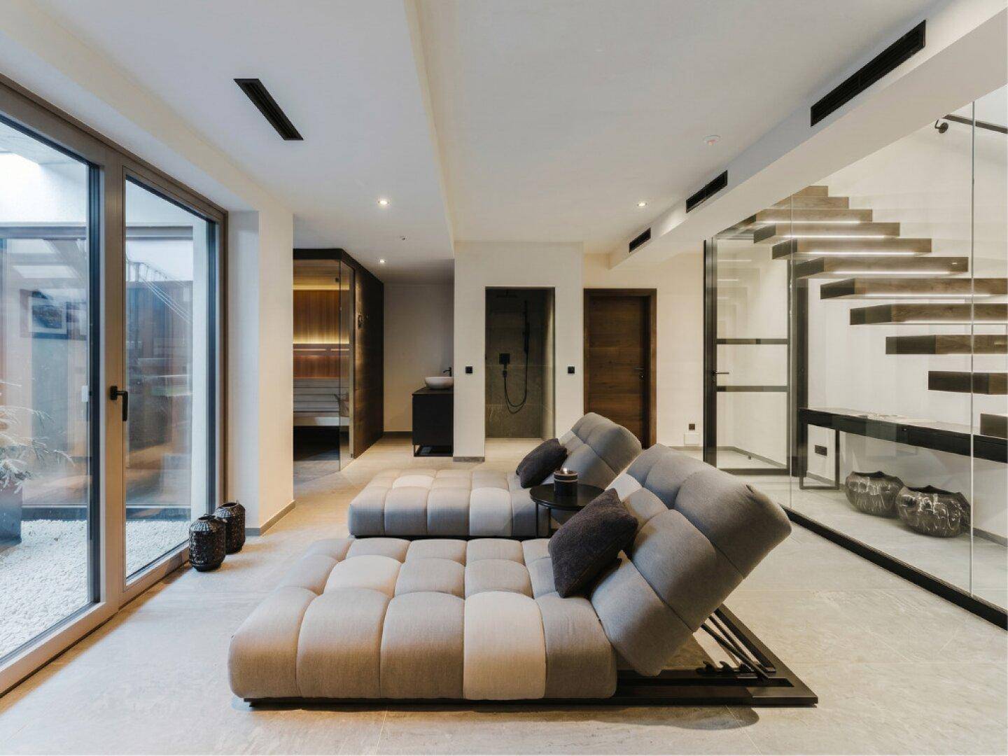 Exklusiver Wellnessbereich mit Liegen, Glas-Treppe und Sauna, bietet direkten Zugang nach draußen.