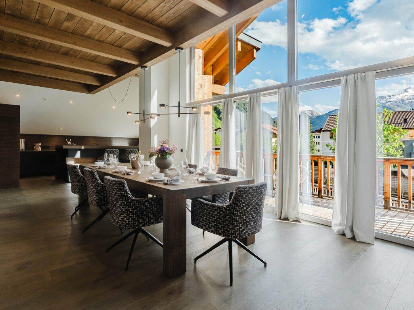 Eleganter Essbereich mit Holztisch, hohen Decken und Zugang zu einem Balkon mit Bergblick.