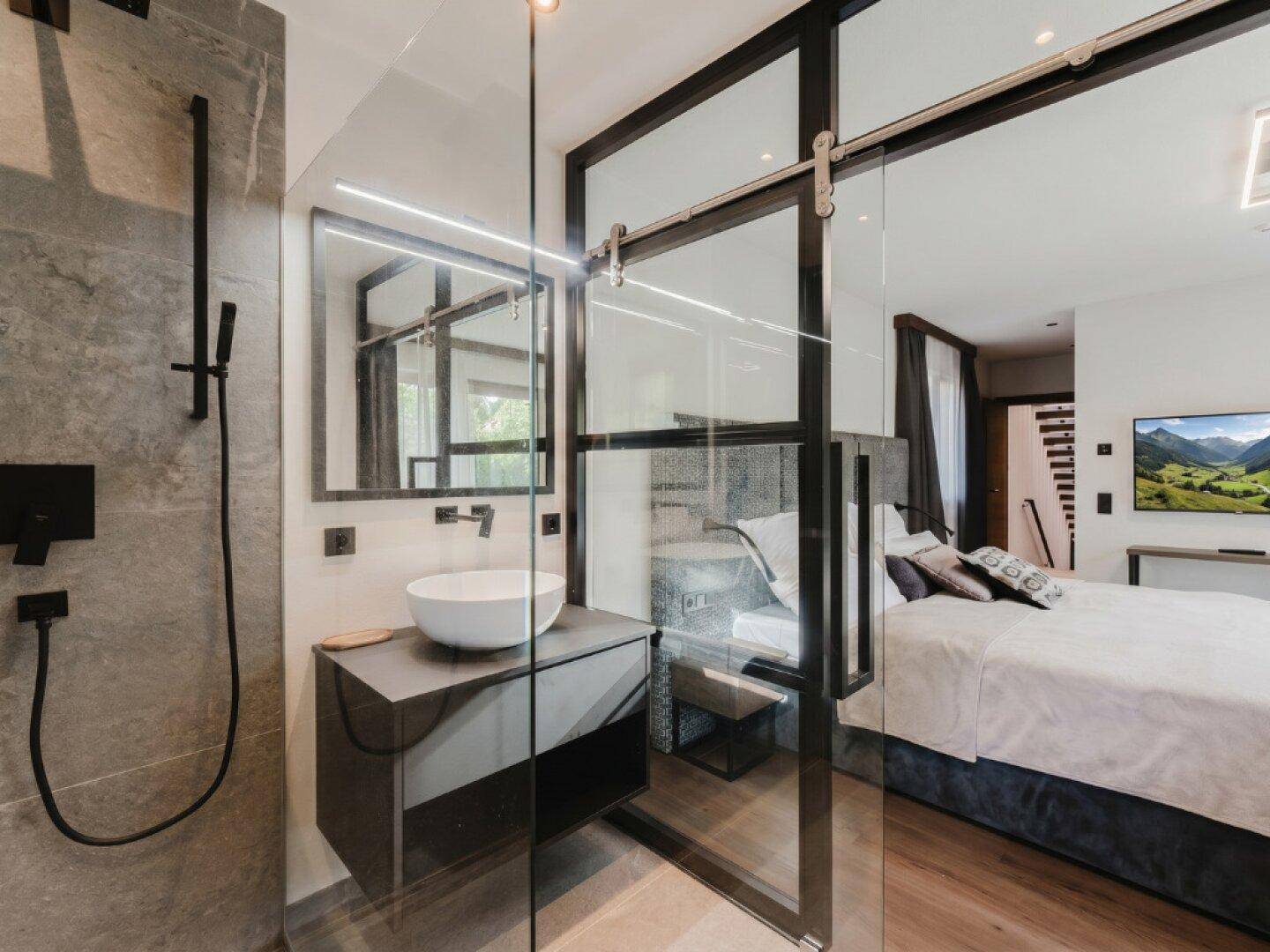 Modernes Bad mit begehbarer Dusche und Waschbecken, durch Glasschiebetür vom Schlafzimmer getrennt.