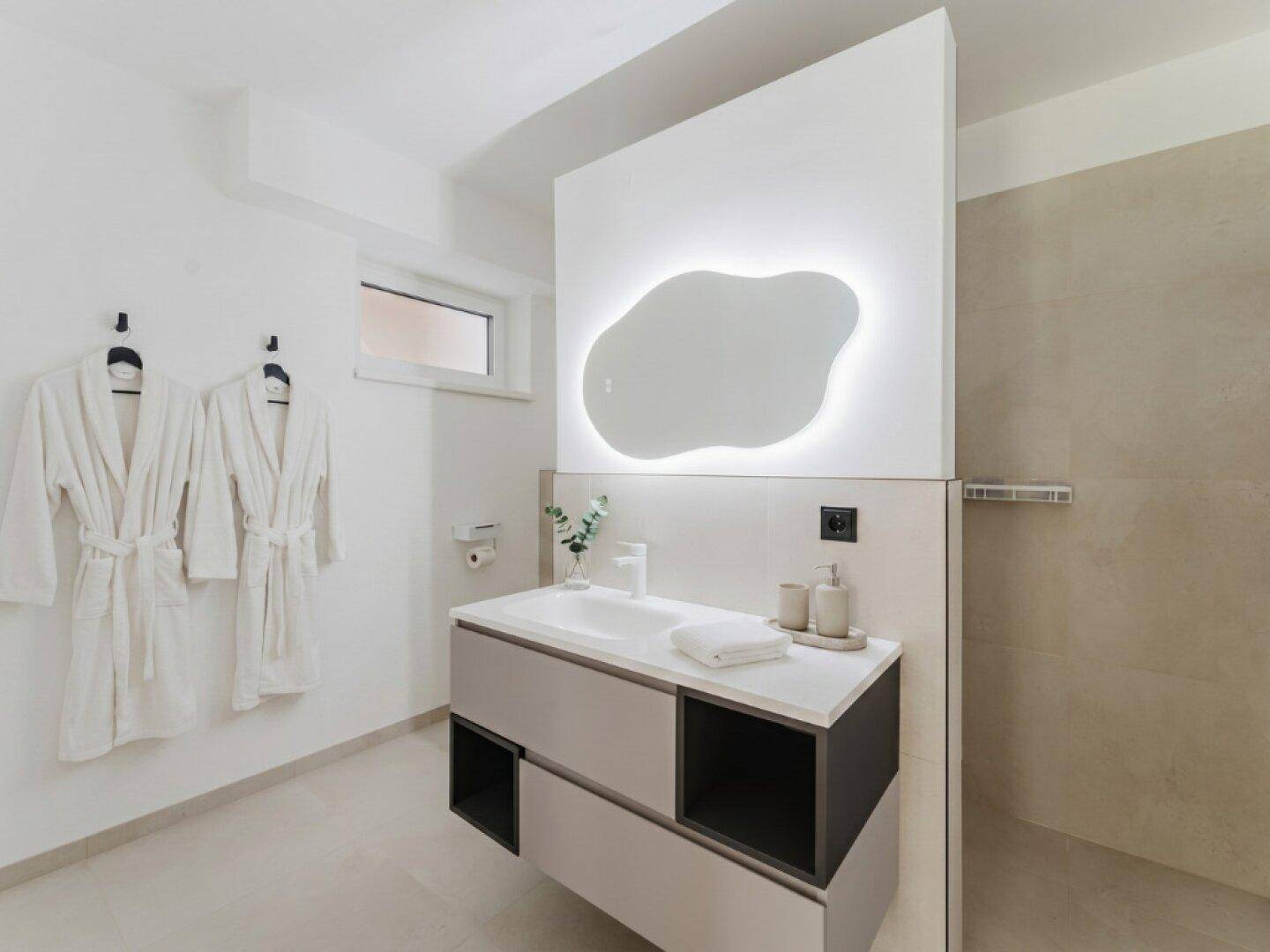 Modernes Badezimmer mit Waschtisch, beleuchtetem Spiegel und Duschbereich.