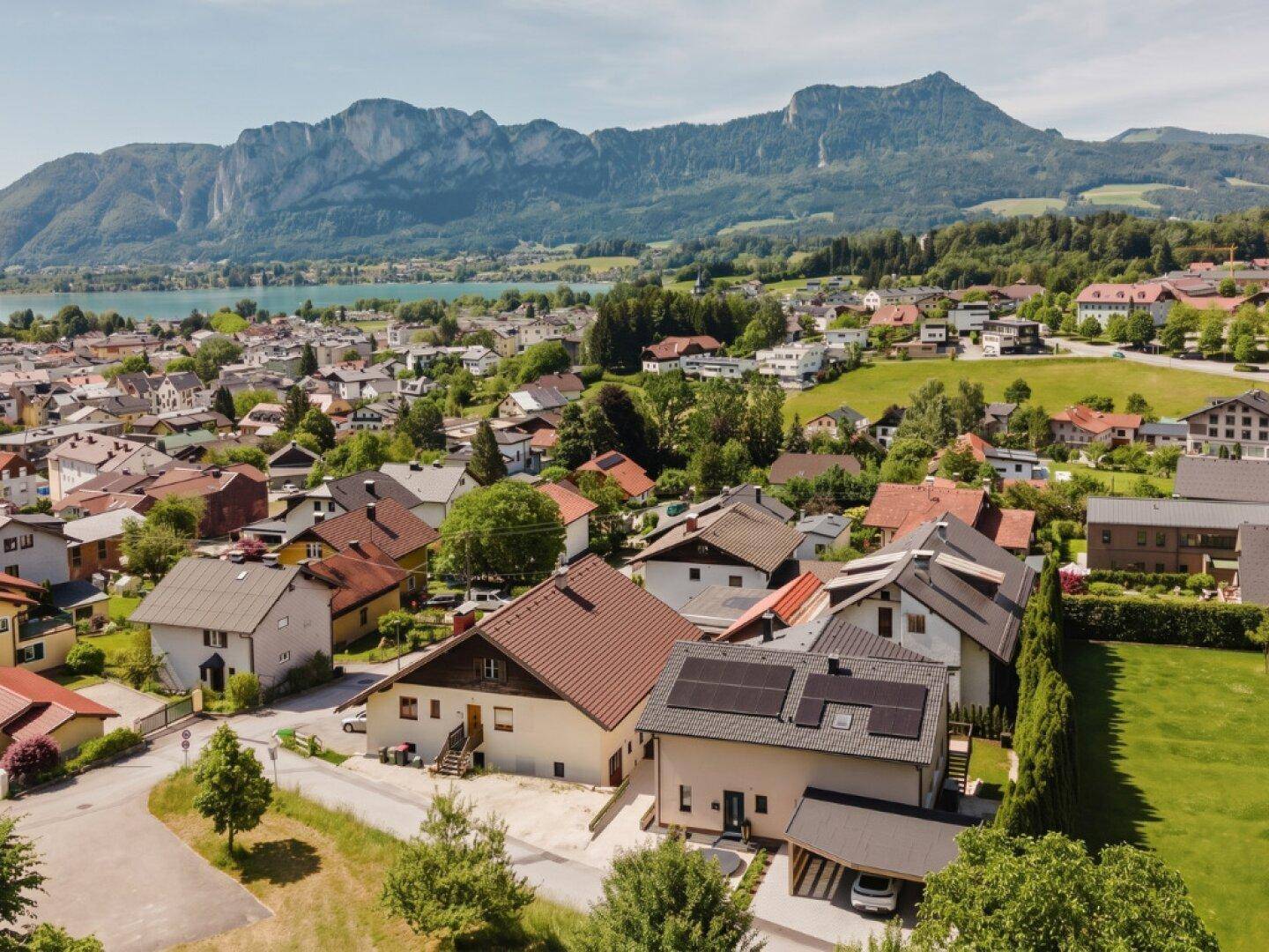 Luftaufnahme einer Wohnsiedlung mit See- und Bergblick, einige Häuser mit Solaranlagen.