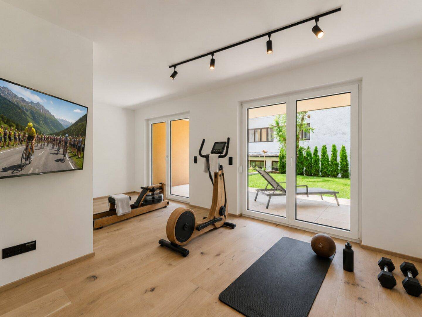 Fitnessraum mit Trainingsgeräten, Fernseher und direktem Zugang zur Terrasse.