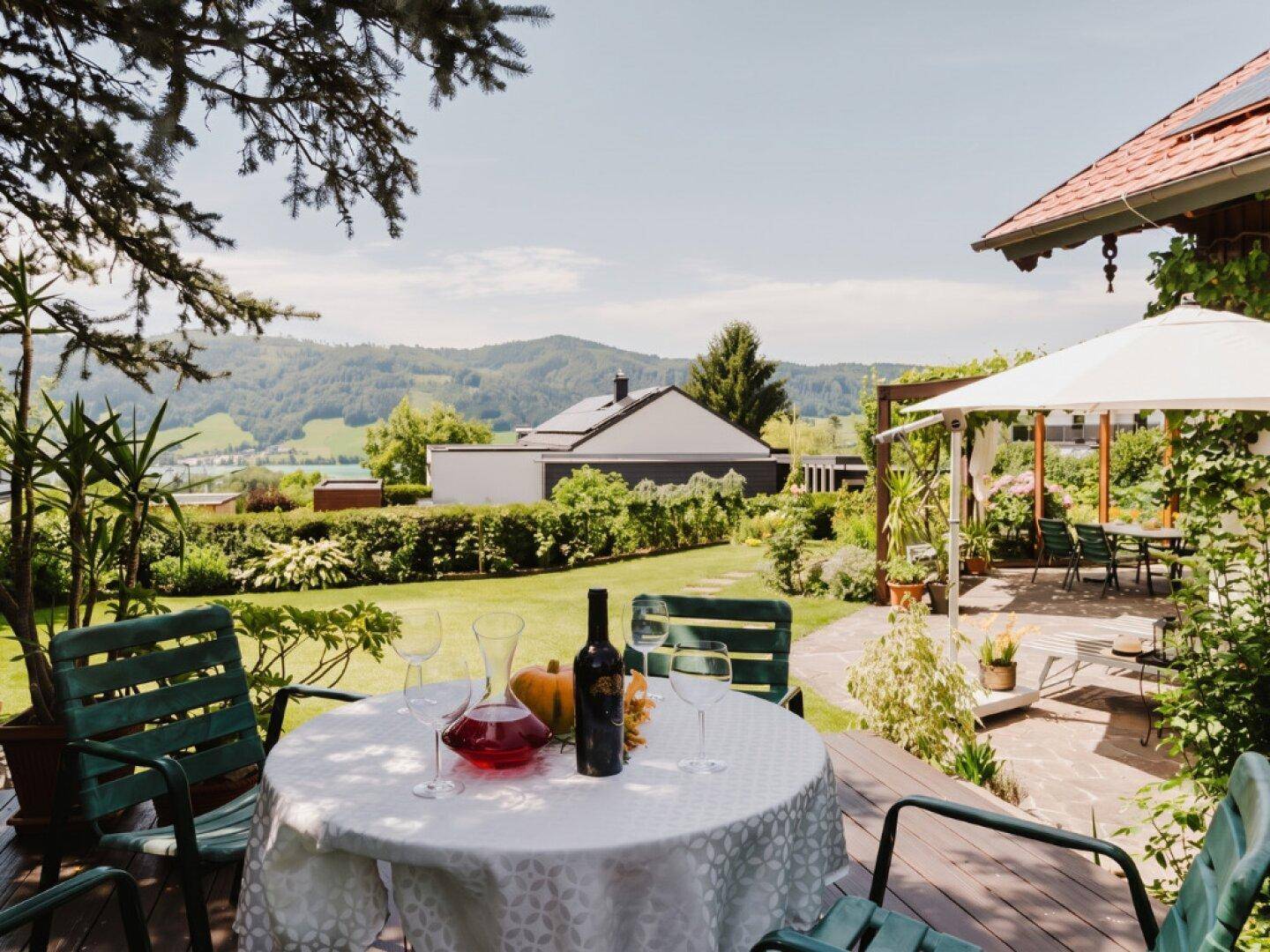 Gemütliche Terrasse mit Esstisch und weitem Blick über die grüne Landschaft und Berge.