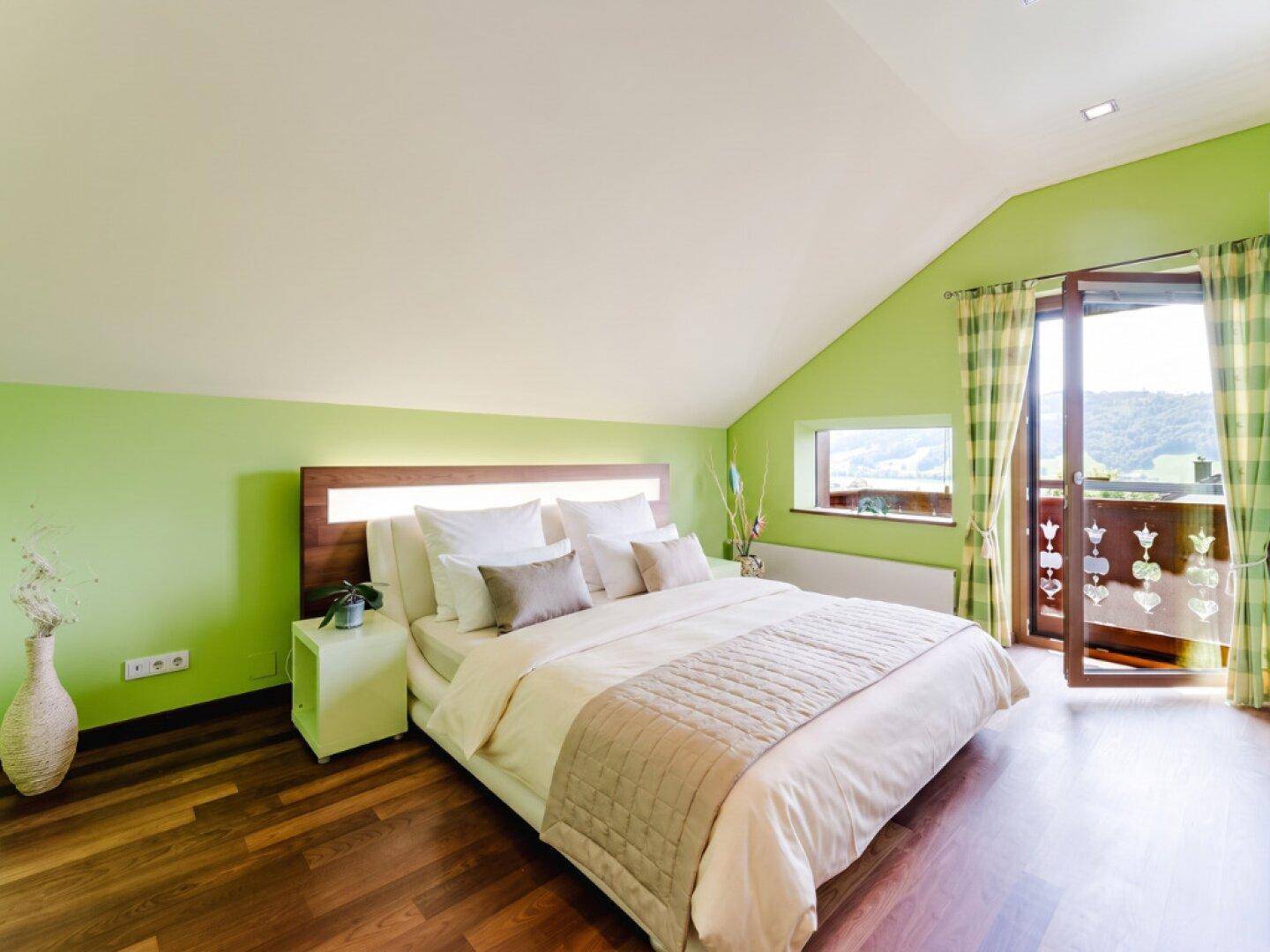 Modernes Schlafzimmer im Dachgeschoss mit Balkonzugang und grünen Wänden.