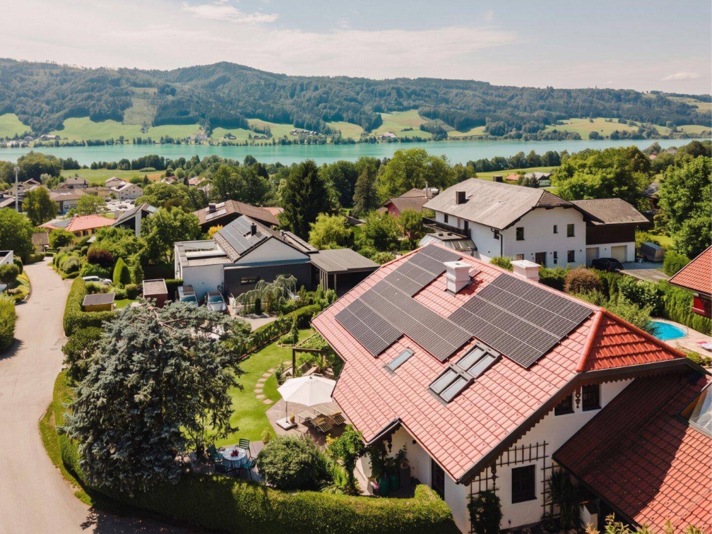 Luftaufnahme des Hauses mit Photovoltaikanlage, Garten und Blick auf den See und die Berge.