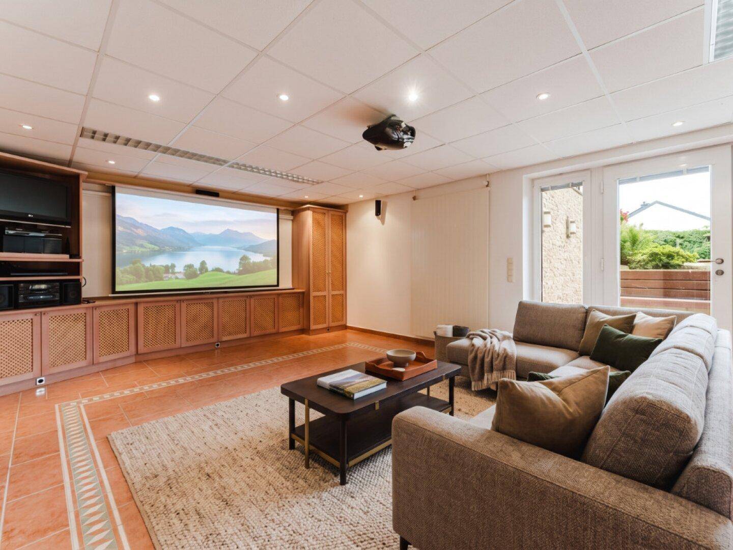 Geräumiger Medienraum mit Heimkino, bequemen Sofas und Zugang zur Terrasse.