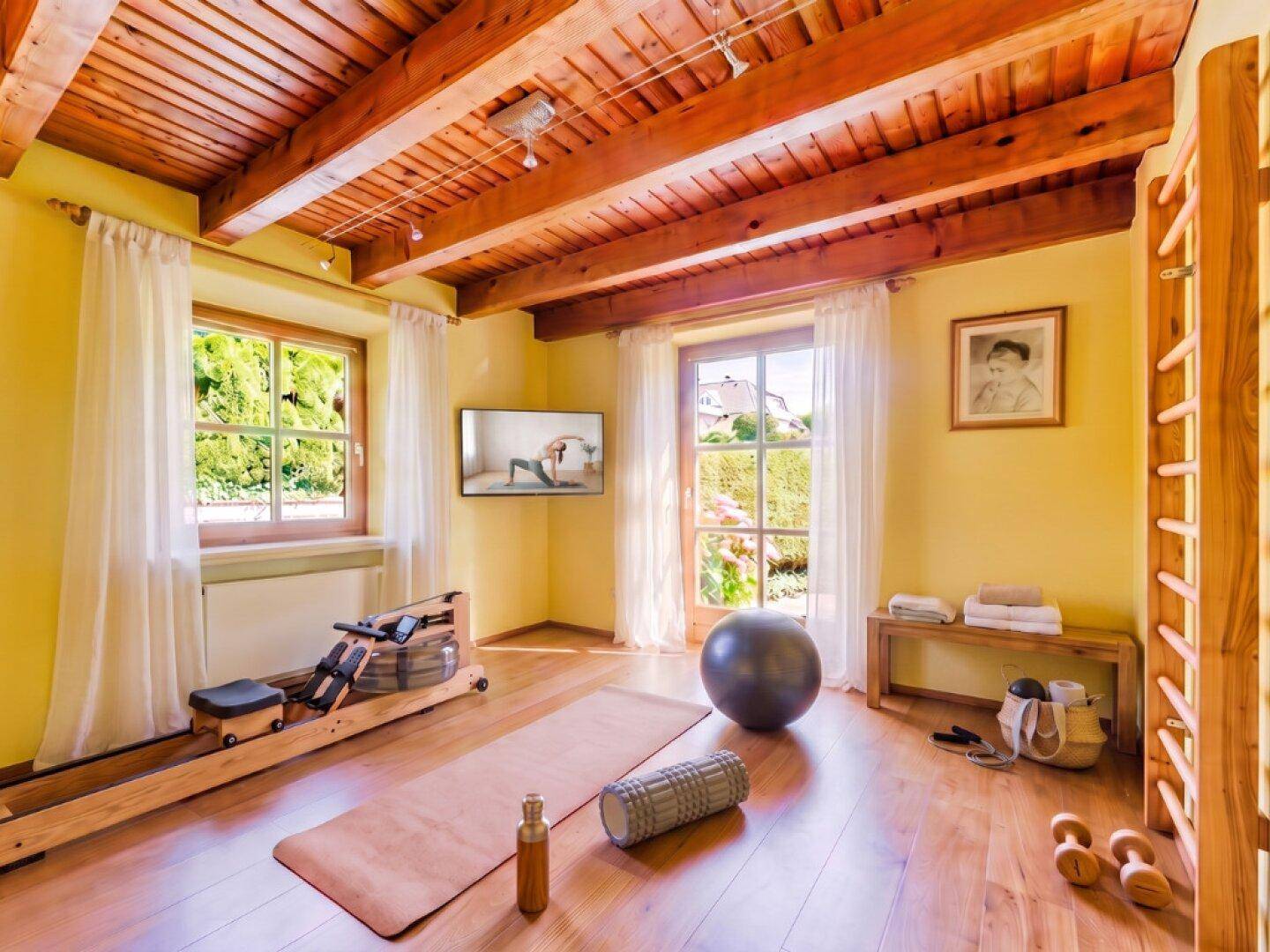 Heller Fitnessraum mit Holzbalkendecke, Parkettboden und Blick in den Garten.