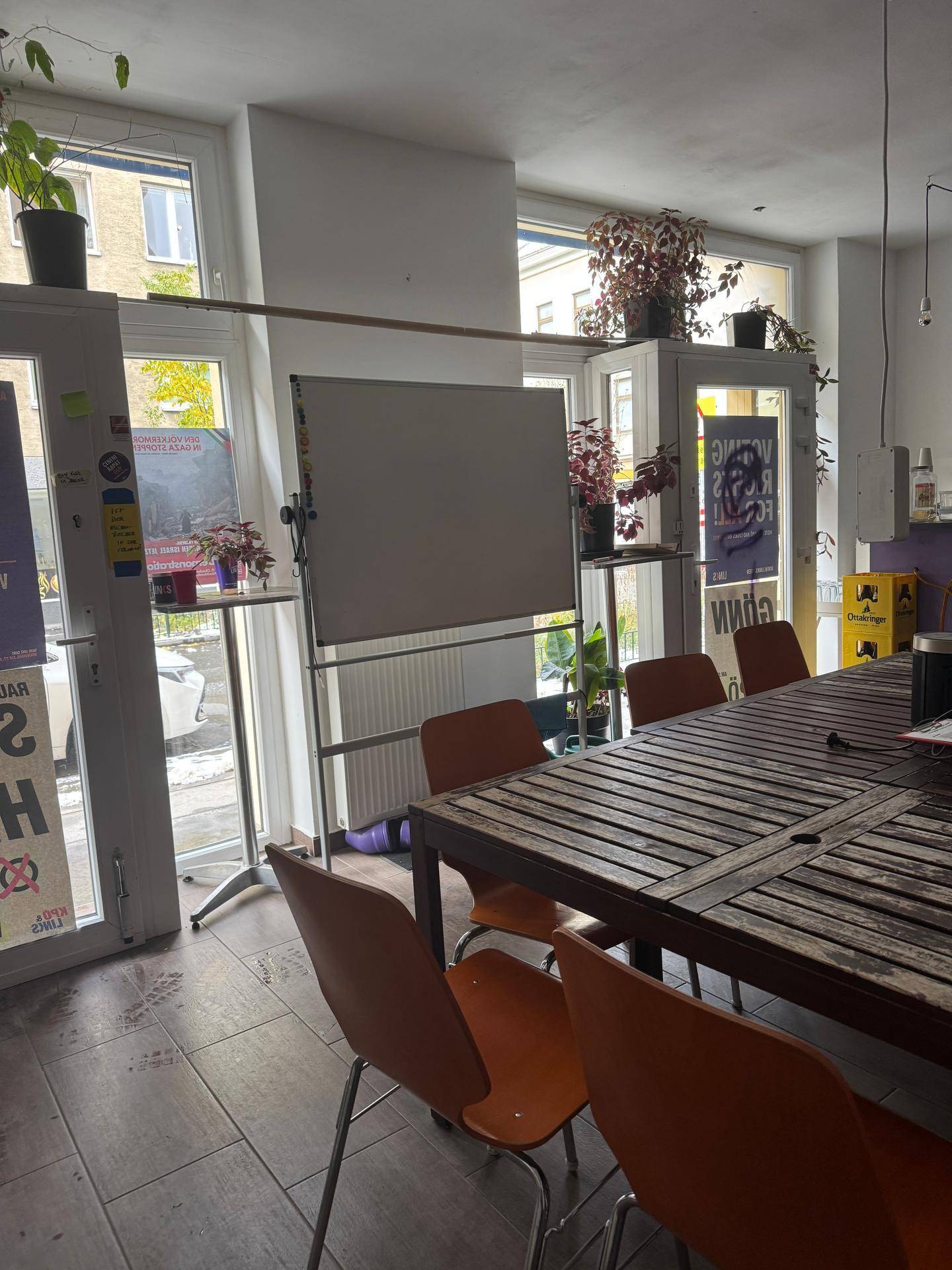 Heller Raum mit großem Holztisch, Stühlen und Whiteboard, viel Tageslicht durch große Fenster.