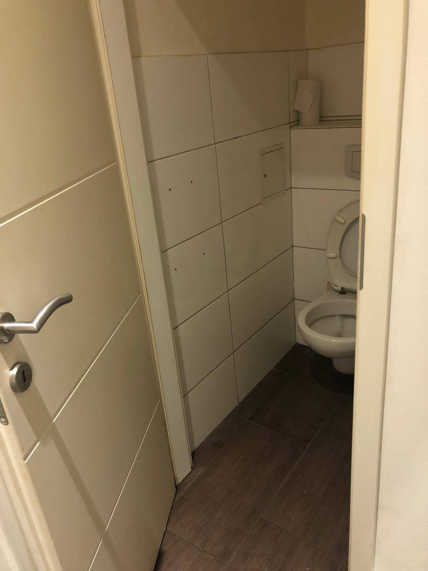 Kleiner Toilettenraum mit weißen Fliesen an den Wänden und dunklem Fliesenboden.