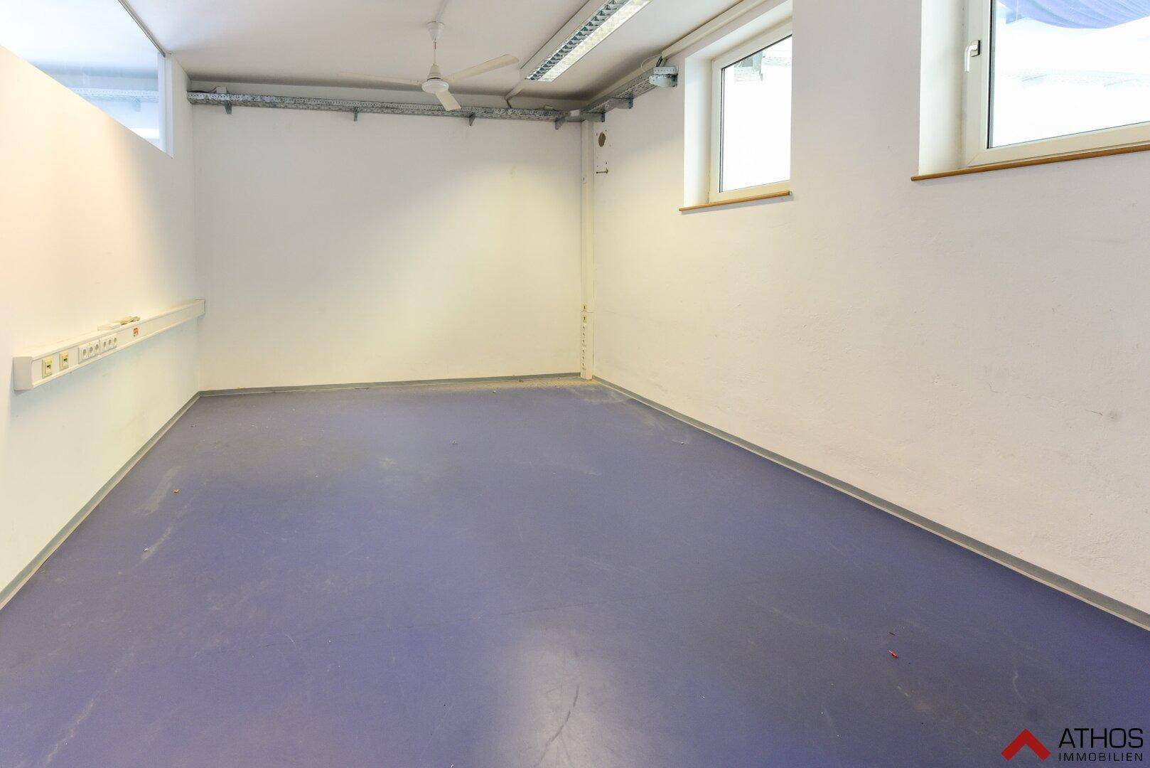 Kleinerer Raum mit lila Vinylboden, weißen Wänden und zwei Fenstern.