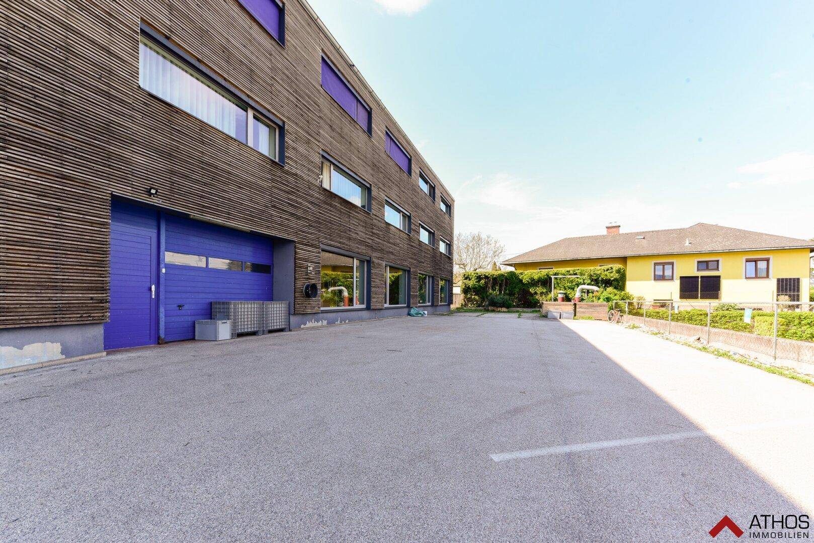 Seitenansicht eines modernen Geschäftsgebäudes mit Holzfassade und einem großen, asphaltierten Parkplatz.