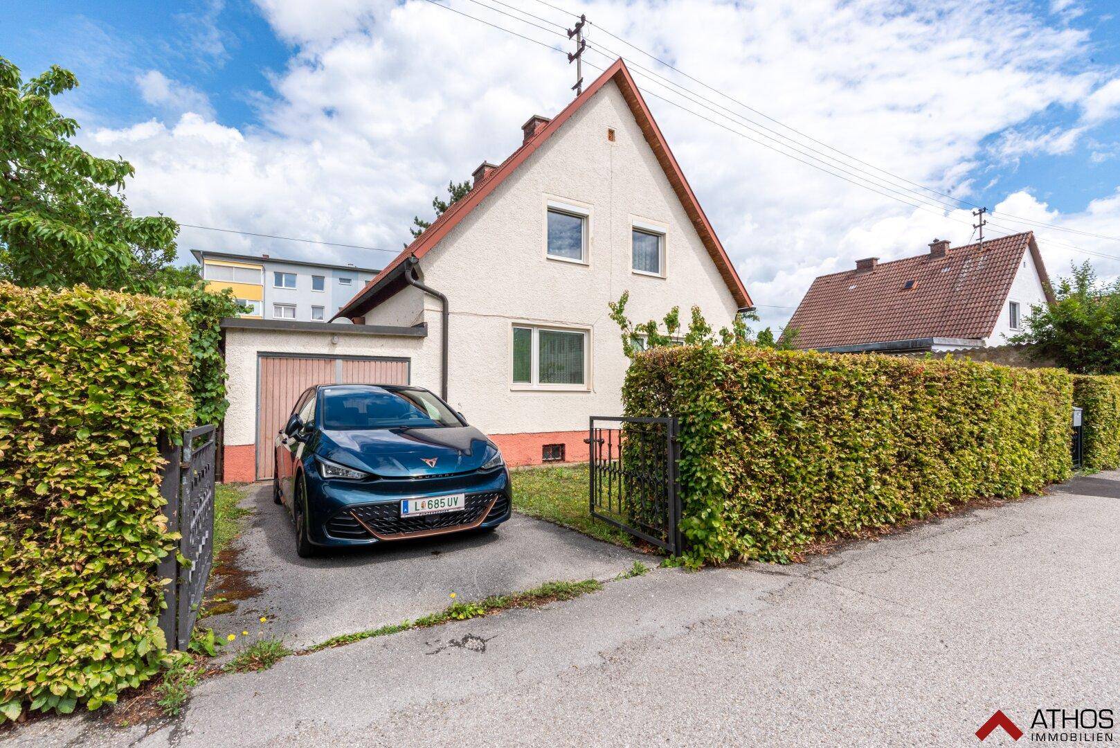 Seitenansicht des Hauses mit Einfahrt, Garage und einem gepflegten Vorgarten mit Hecke.