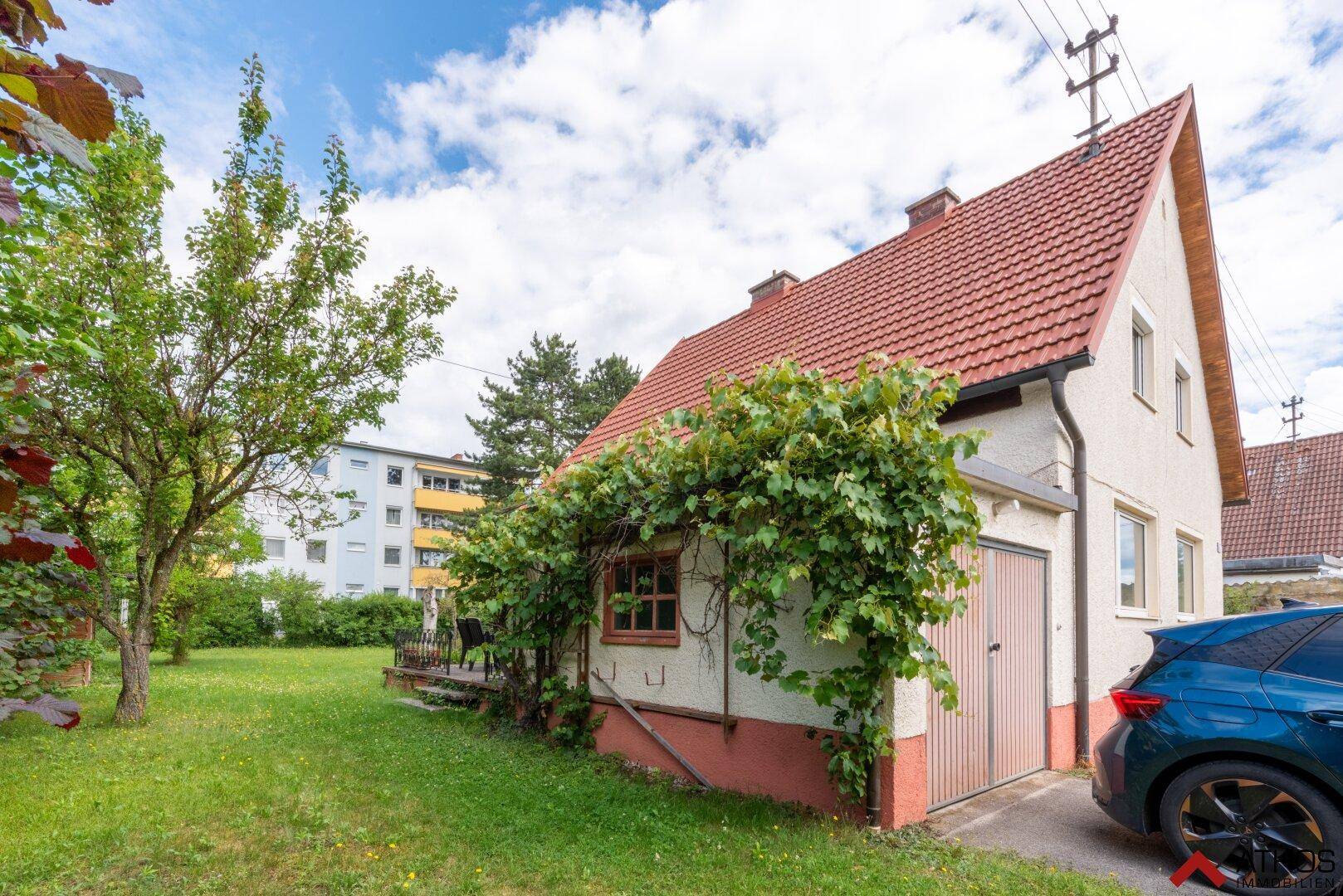 Seitenansicht des Hauses mit Garage, umrankt von Pflanzen, und einem kleinen Gartenbereich.