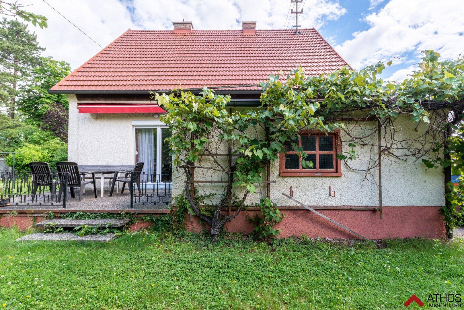 Hinteransicht des Hauses mit einer möblierten Terrasse und einem weitläufigen, grünen Garten.