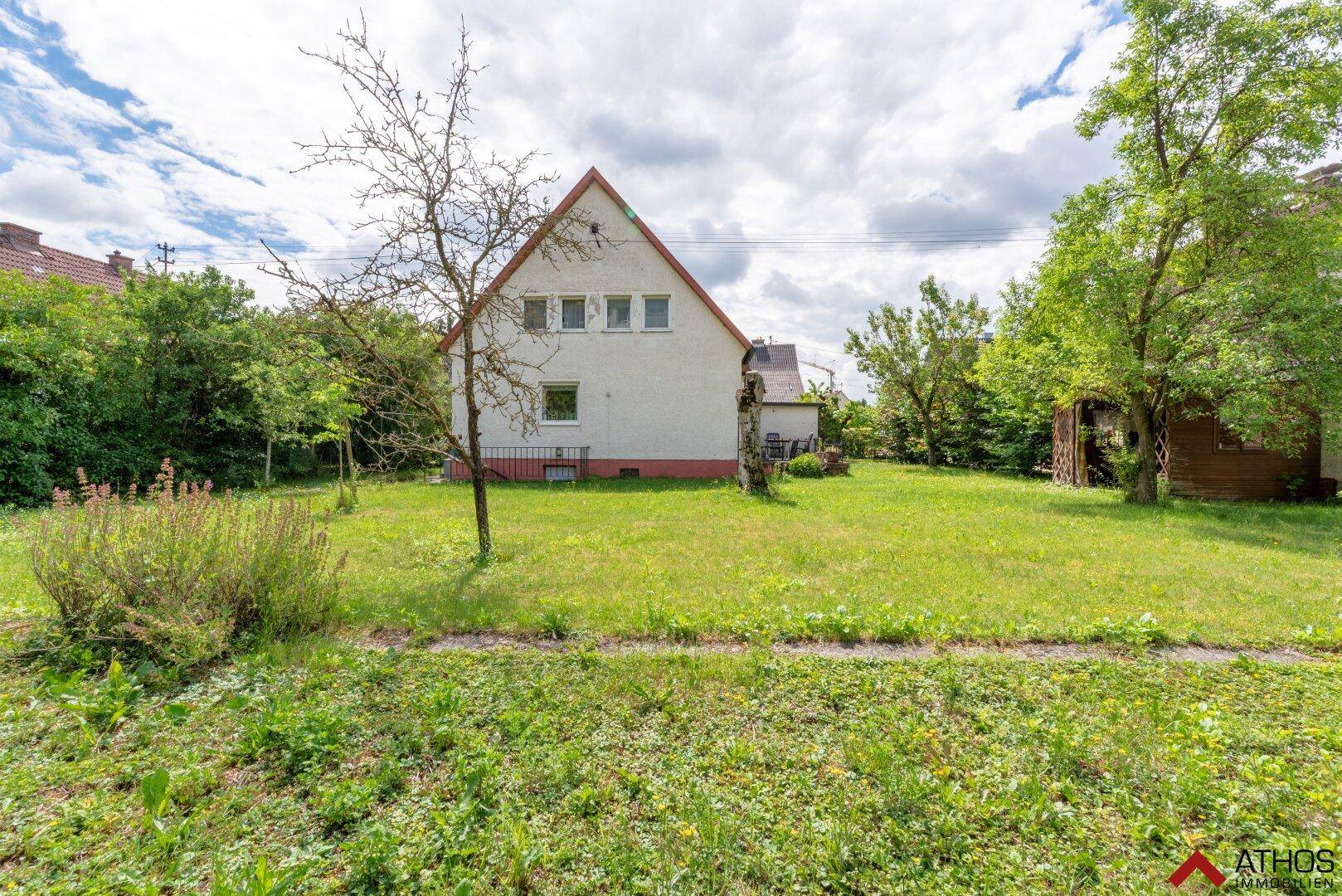 Großer, offener Gartenbereich hinter dem Haus mit viel Grün und einzelnen Bäumen.