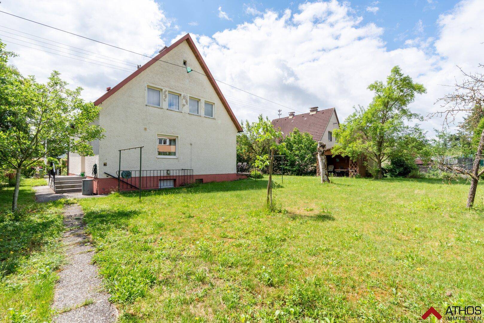 Weitläufiger Garten mit Rasenfläche und Bäumen, der sich hinter dem Einfamilienhaus erstreckt.
