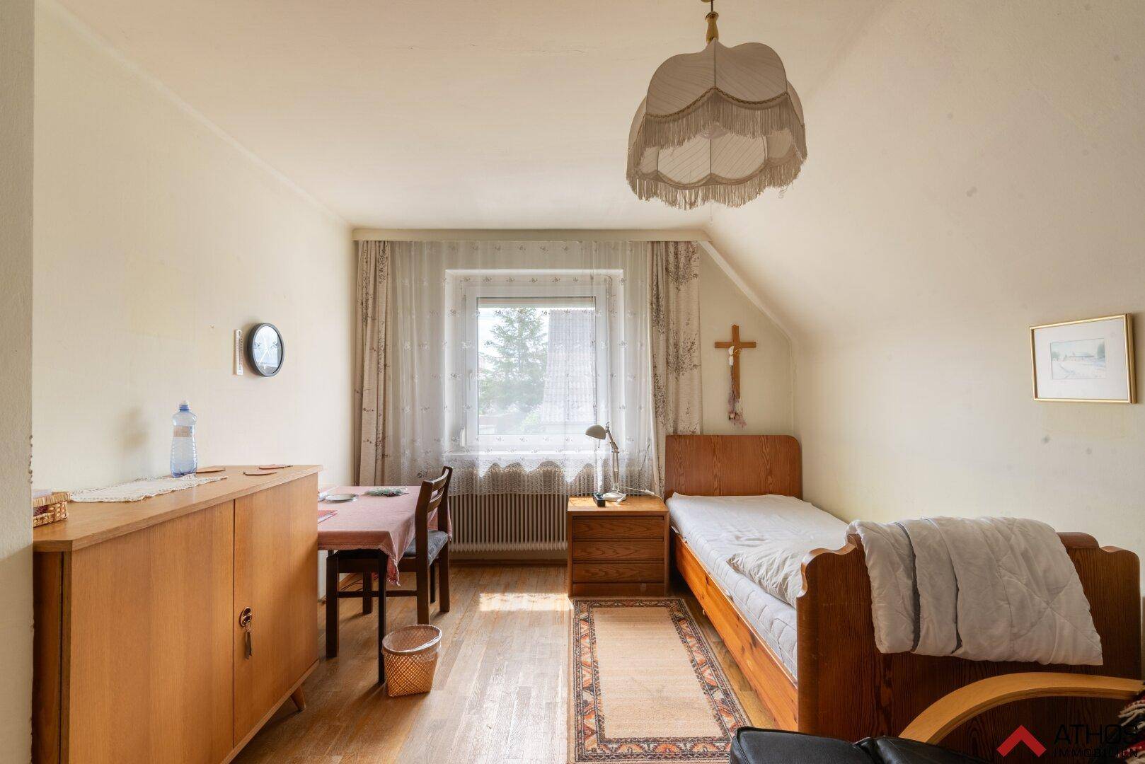 Helles Schlafzimmer mit Holzboden, Einzelbett und einem Fenster mit Blick ins Grüne.