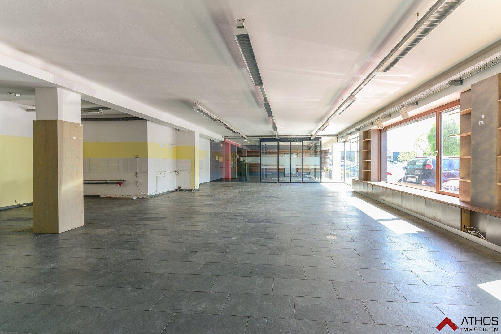 Geräumige, leere Gewerbefläche mit großen Fenstern und Fliesenboden, bereit für den Ausbau.
