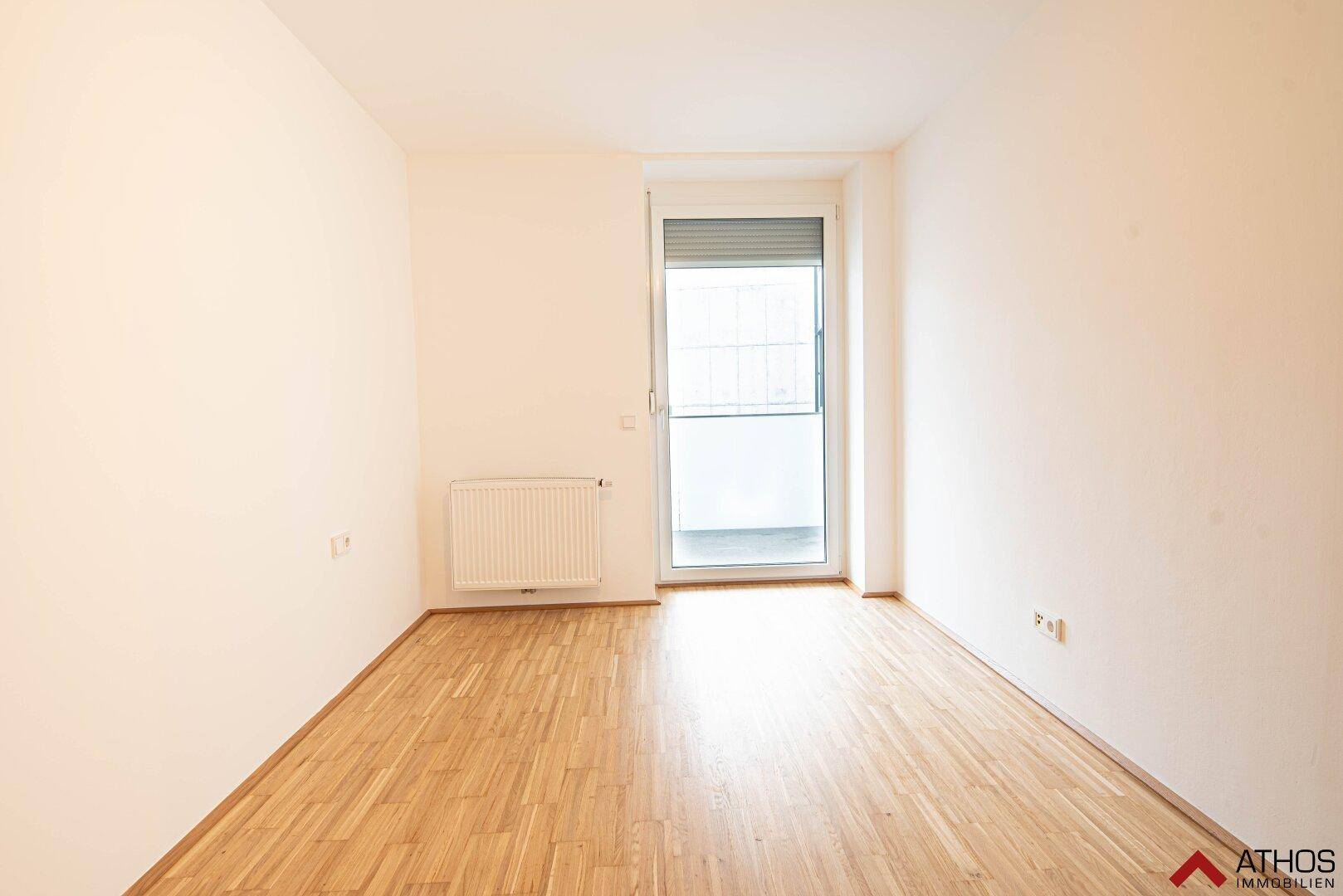 Helles Zimmer mit Parkettboden und Zugang zu einem Balkon, ideal als Schlaf- oder Wohnbereich.