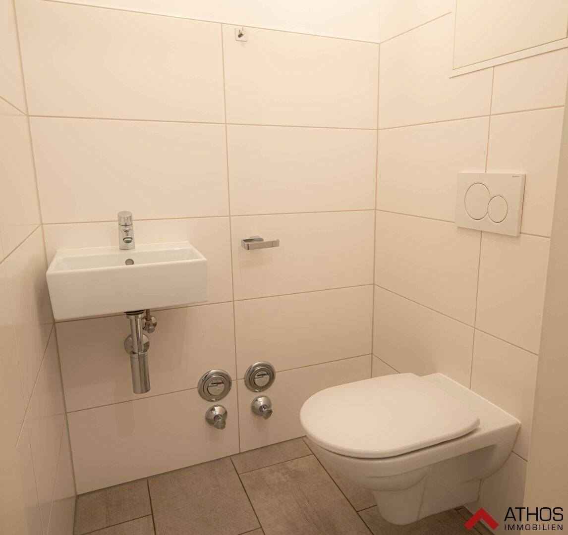 Modernes Gäste-WC mit wandhängender Toilette und kleinem Waschbecken, in hellen Fliesen gehalten.