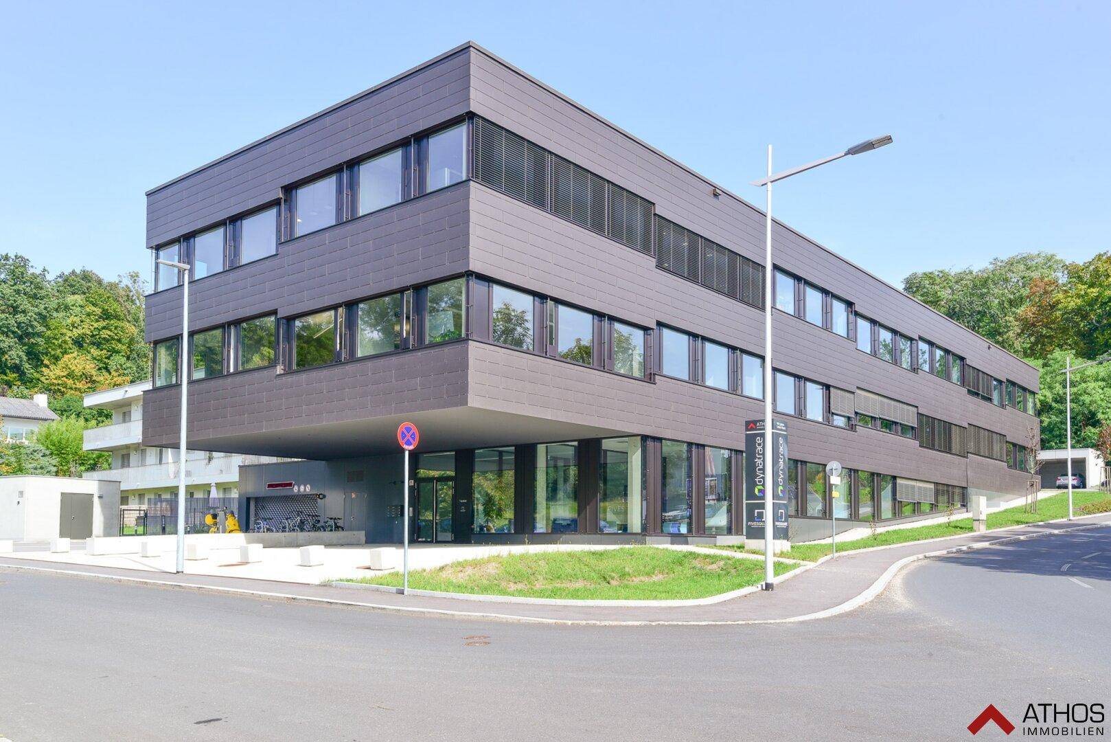 Modernes Bürogebäude mit dunkler Fassade und großen Fensterfronten in einer grünen Umgebung.