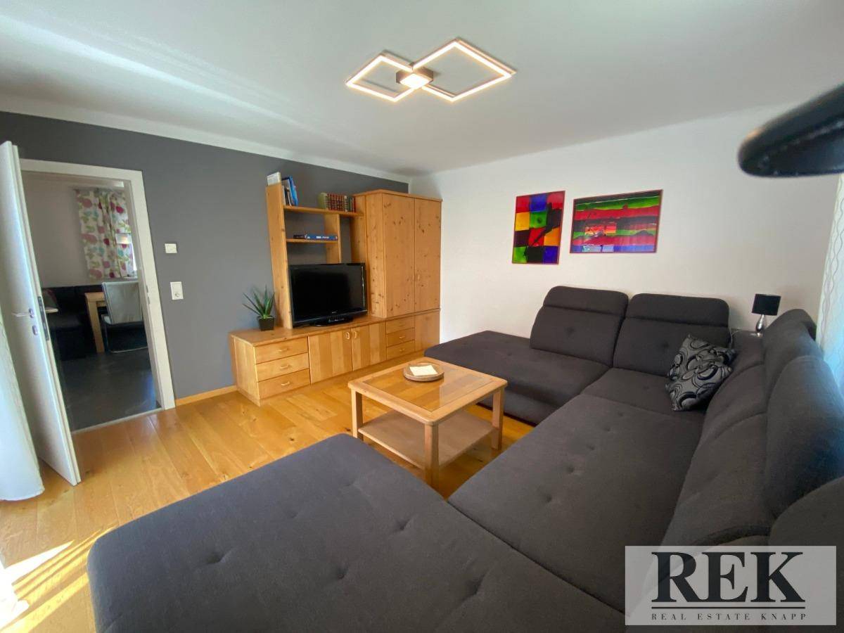 Wohnzimmer mit Ecksofa, Holzmöbeln und Zugang zur Küche.