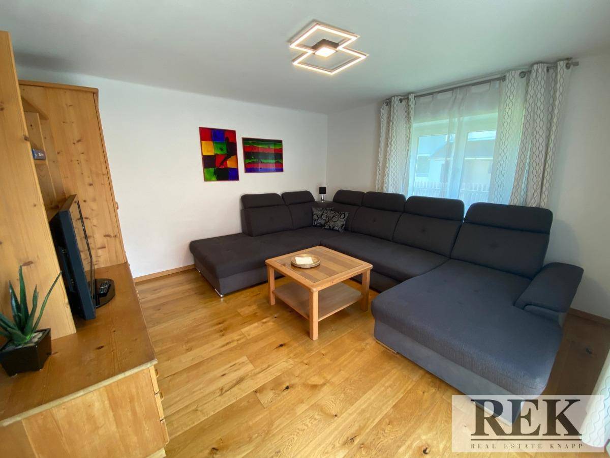 Gemütliches Wohnzimmer mit großem Ecksofa, Holzboden und modernen Deckenleuchten.