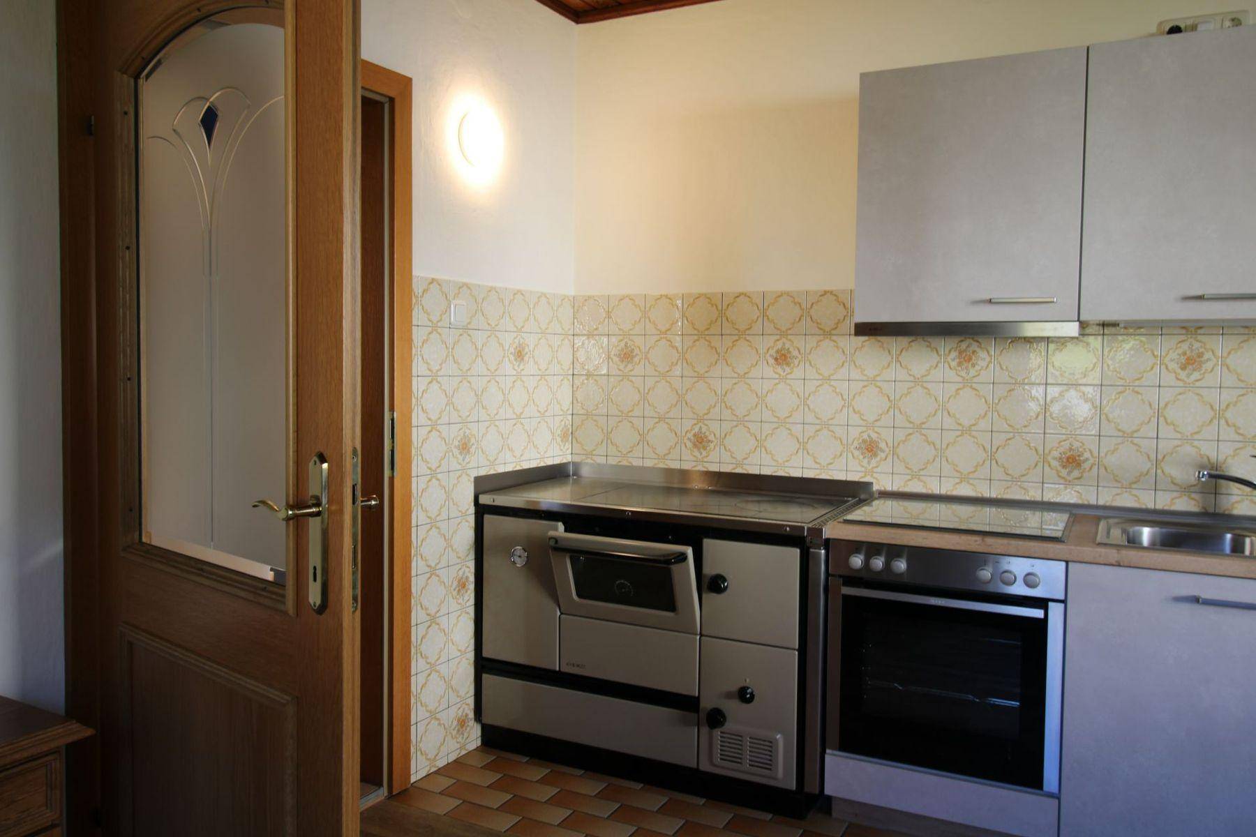 Traditionelle Küche mit Holzofen, Einbaugeräten und gemusterten Wandfliesen.