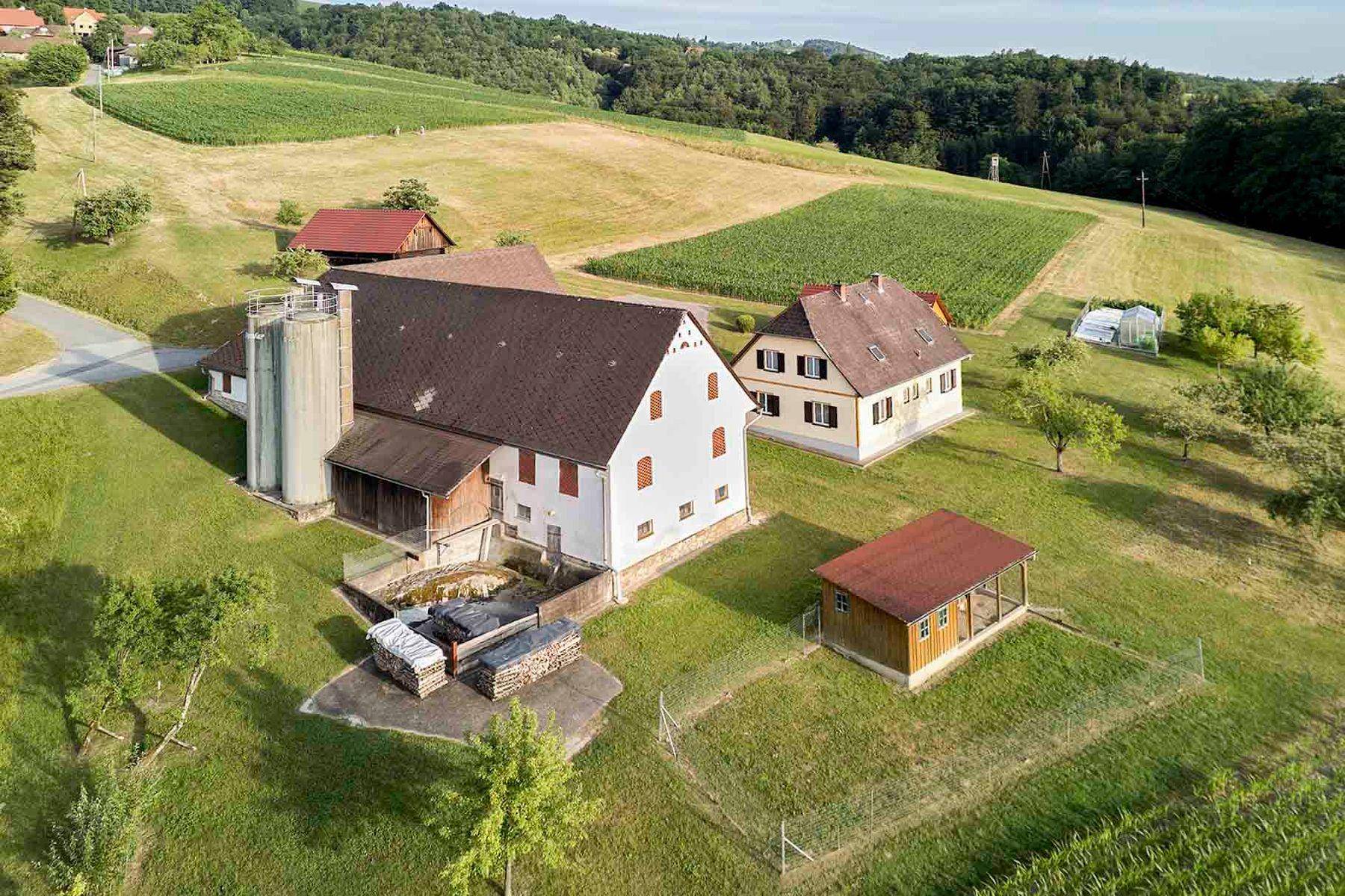 Luftaufnahme des Bauernhofs mit Wohnhaus, Scheunen und umliegenden landwirtschaftlichen Flächen.