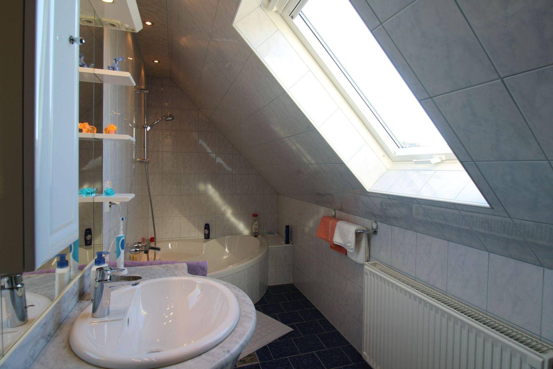 Badezimmer im Dachgeschoss mit Badewanne, Dachfenster und hellen Fliesen.