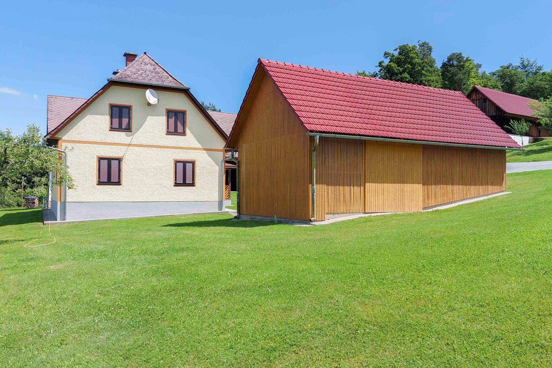 Wohnhaus und ein modernes Holz-Nebengebäude mit rotem Ziegeldach, umgeben von einer grünen Wiese.