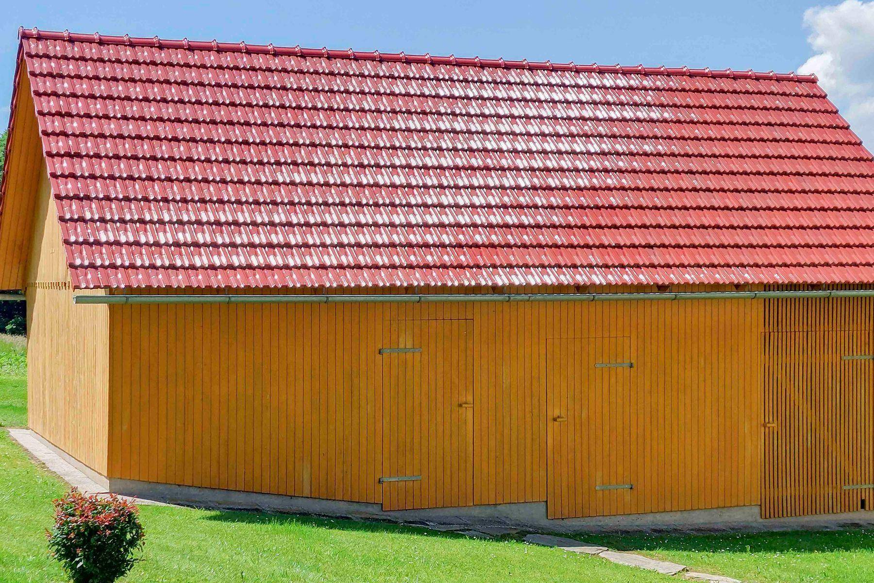 Scheune mit rotem Ziegeldach und holzverkleideter Fassade, umgeben von einer gepflegten Rasenfläche.