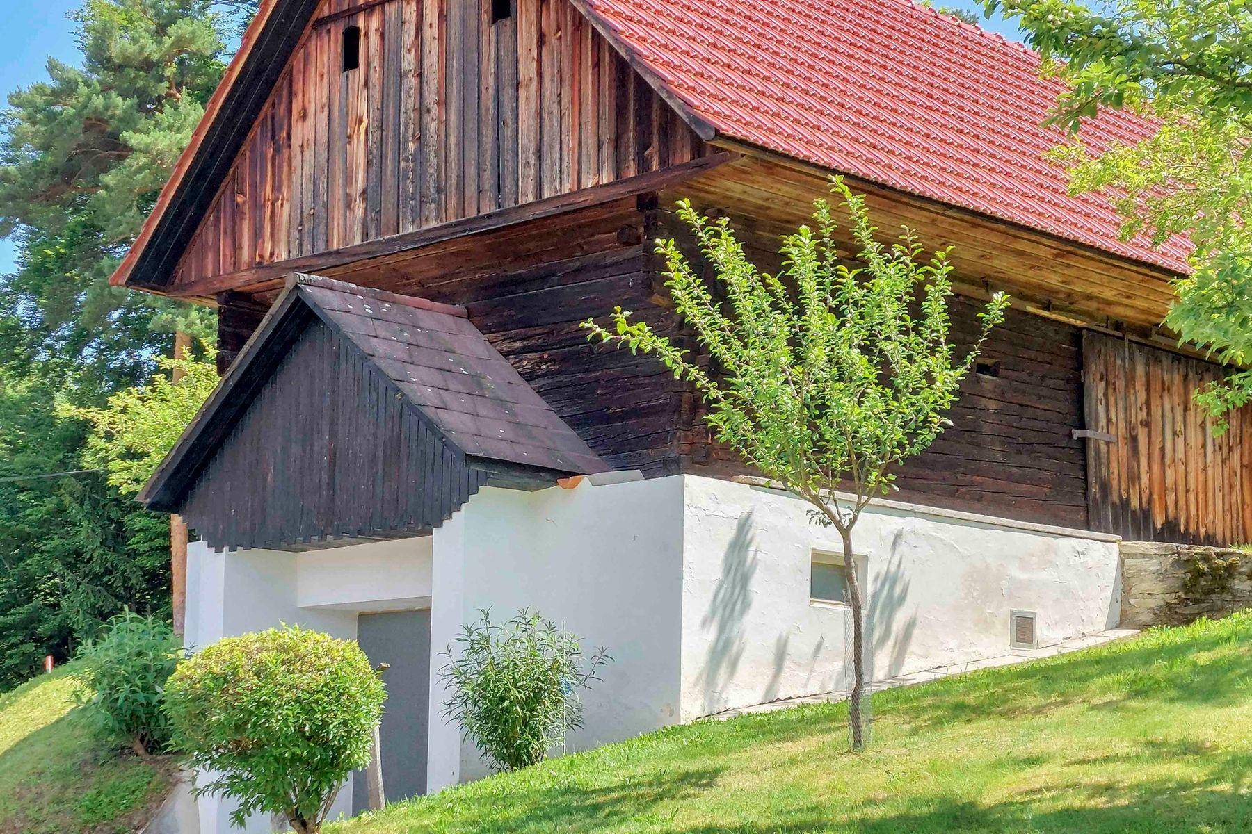Rustikales Gebäude mit dunklen Holzwänden und rotem Ziegeldach, eingebettet in grüne Landschaft.