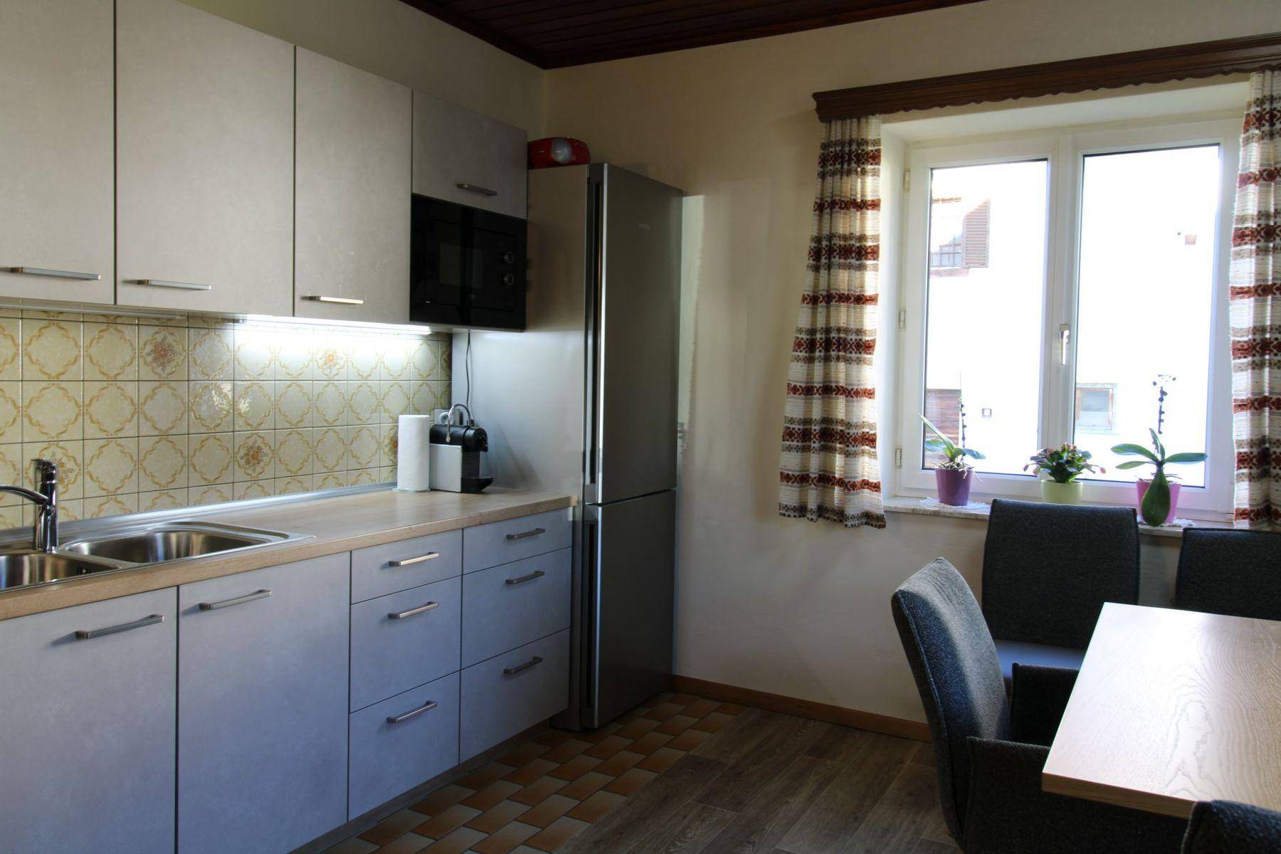 Funktionale Küche mit hellen Schränken, gemusterter Fliesenrückwand und Essbereich am Fenster.