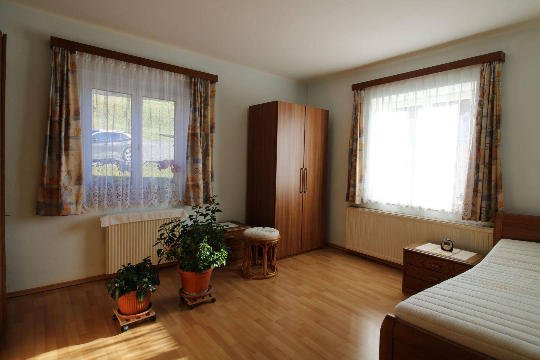 Helles Schlafzimmer mit Holzfußboden, Kleiderschrank und zwei Fenstern, die viel Licht spenden.
