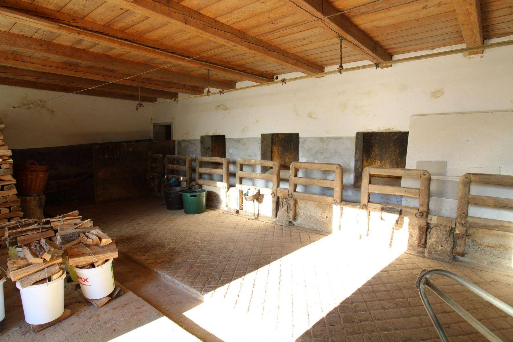 Alter Stallbereich mit Holzbalkendecke, Futterkrippen und viel Tageslicht, das den Raum erhellt.