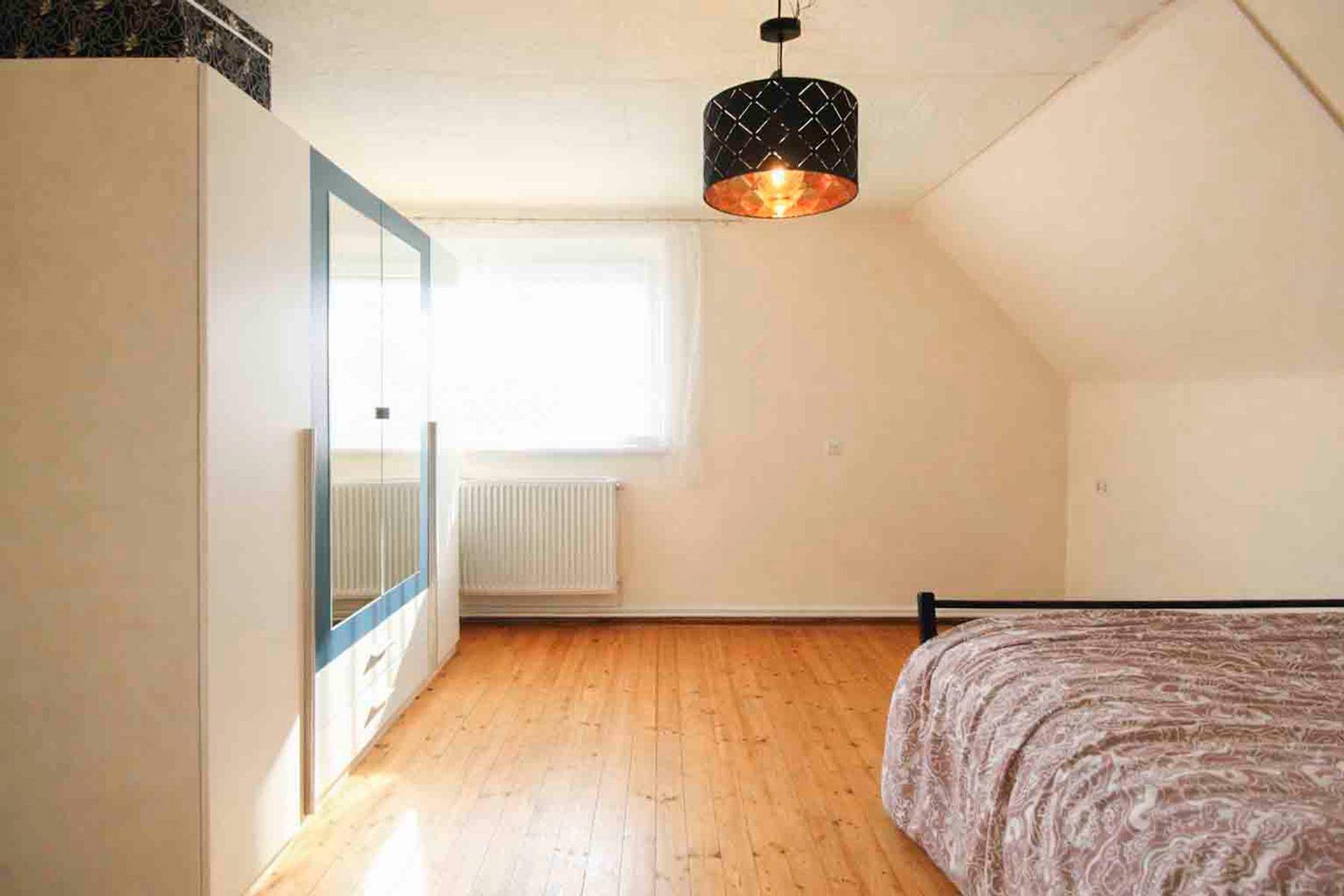 Geräumiges Schlafzimmer im Dachgeschoss mit Holzboden, großem Kleiderschrank und Dachschräge.