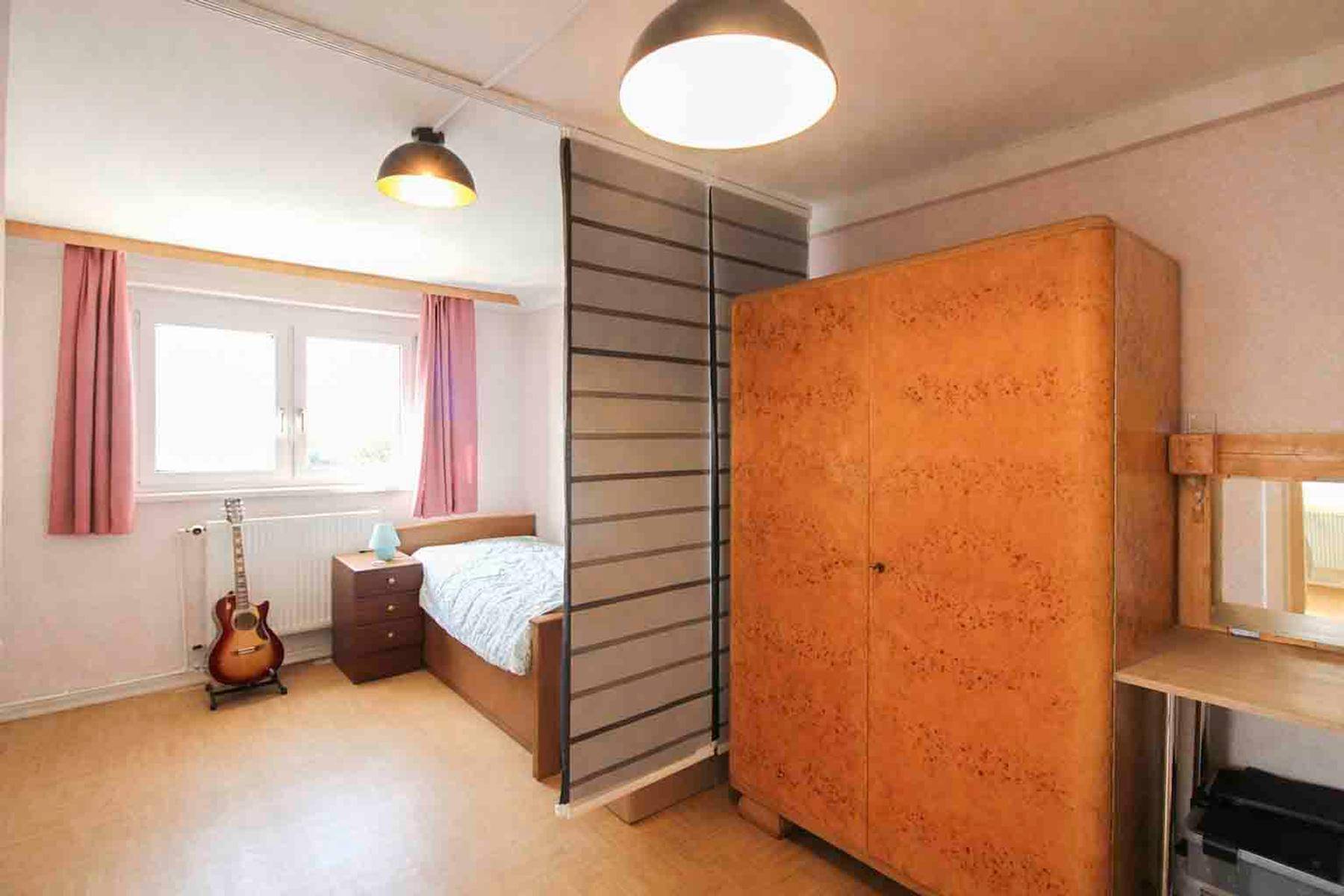 Gemütliches Schlafzimmer mit Holzboden, Fenster und einem Raumteiler für Privatsphäre.