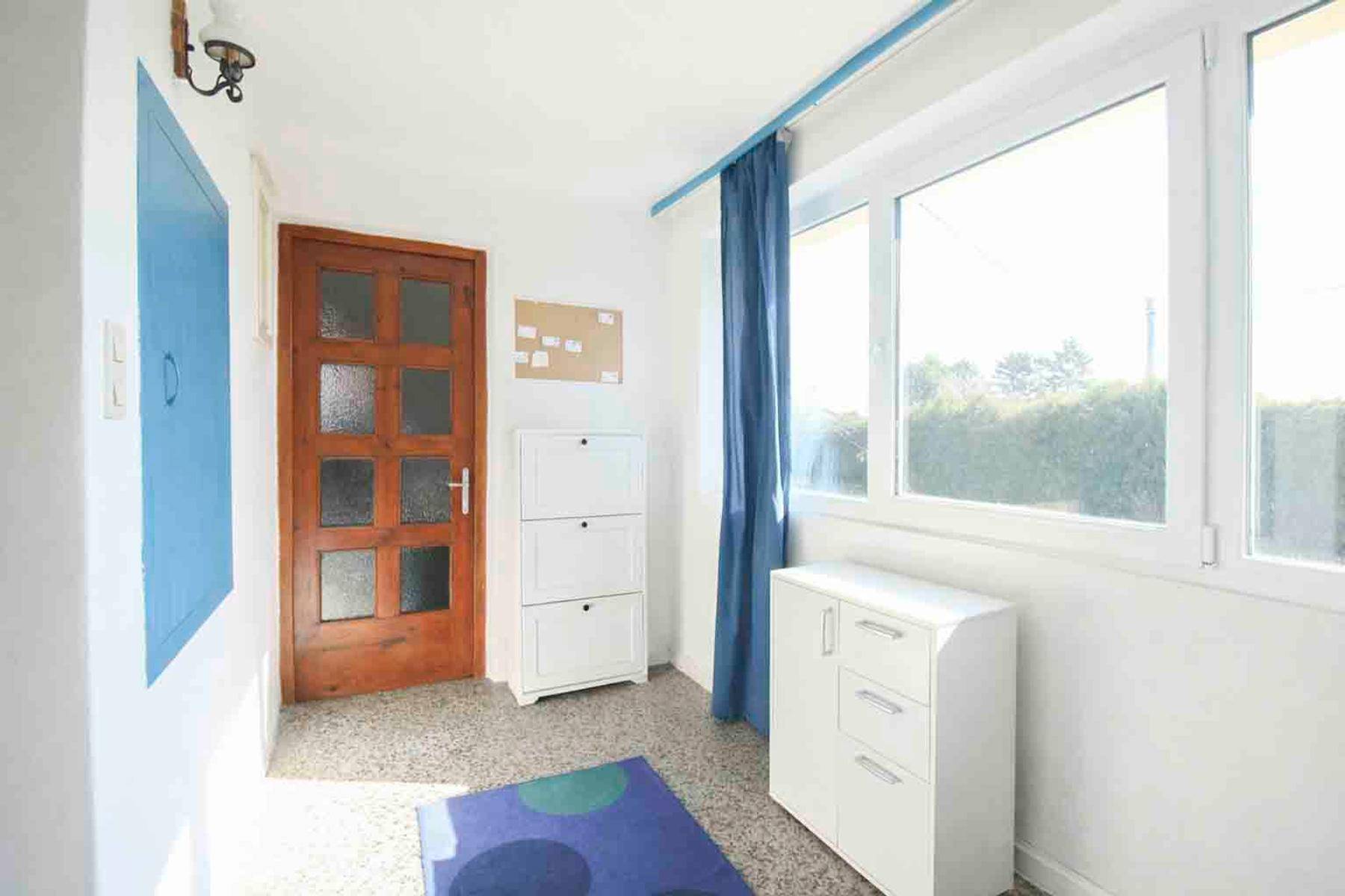 Heller Eingangsbereich mit großen Fenstern, Fliesenboden und Stauraum für Schuhe.