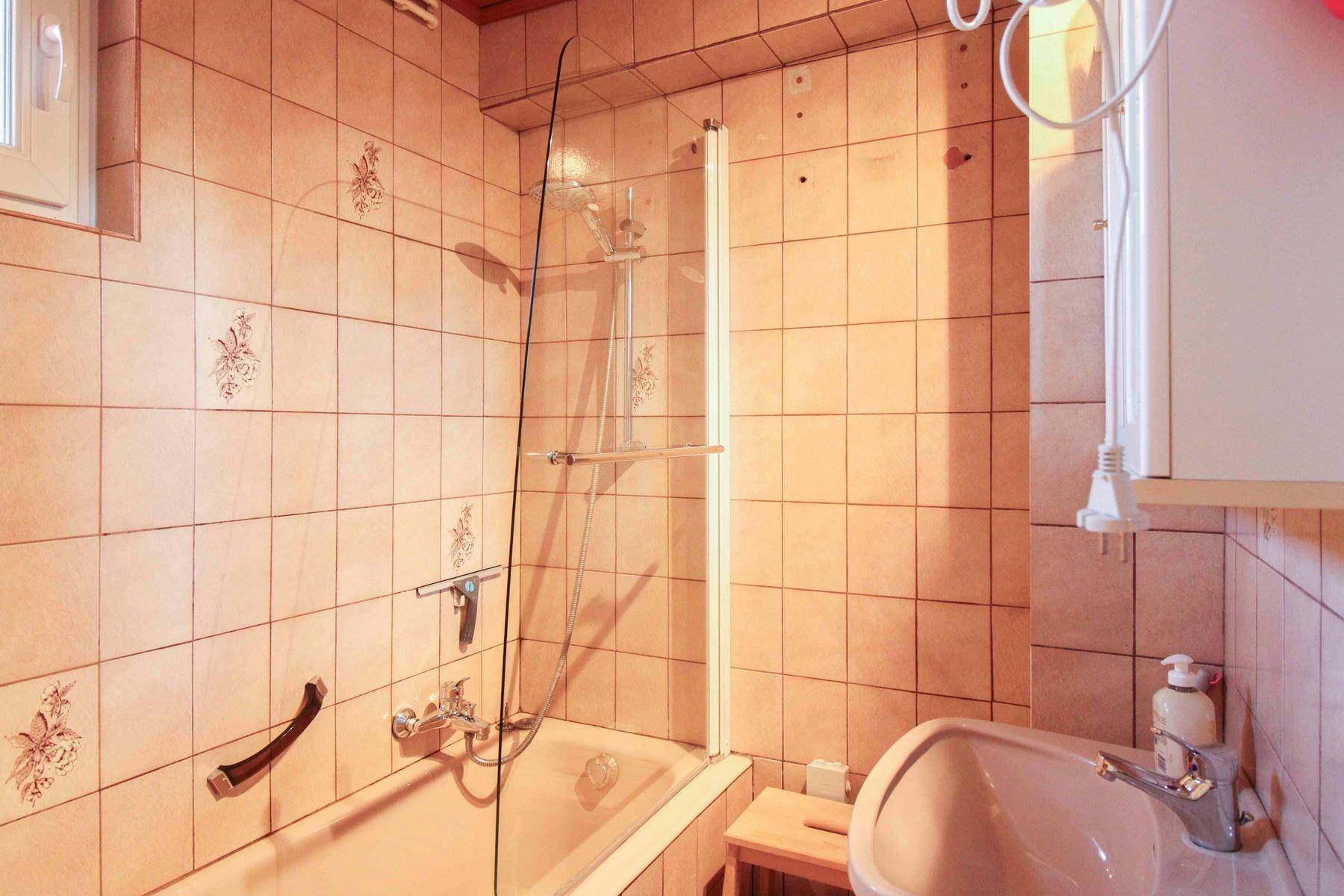 Gefliestes Badezimmer mit Badewanne, Duschabtrennung und Handlauf für mehr Sicherheit.