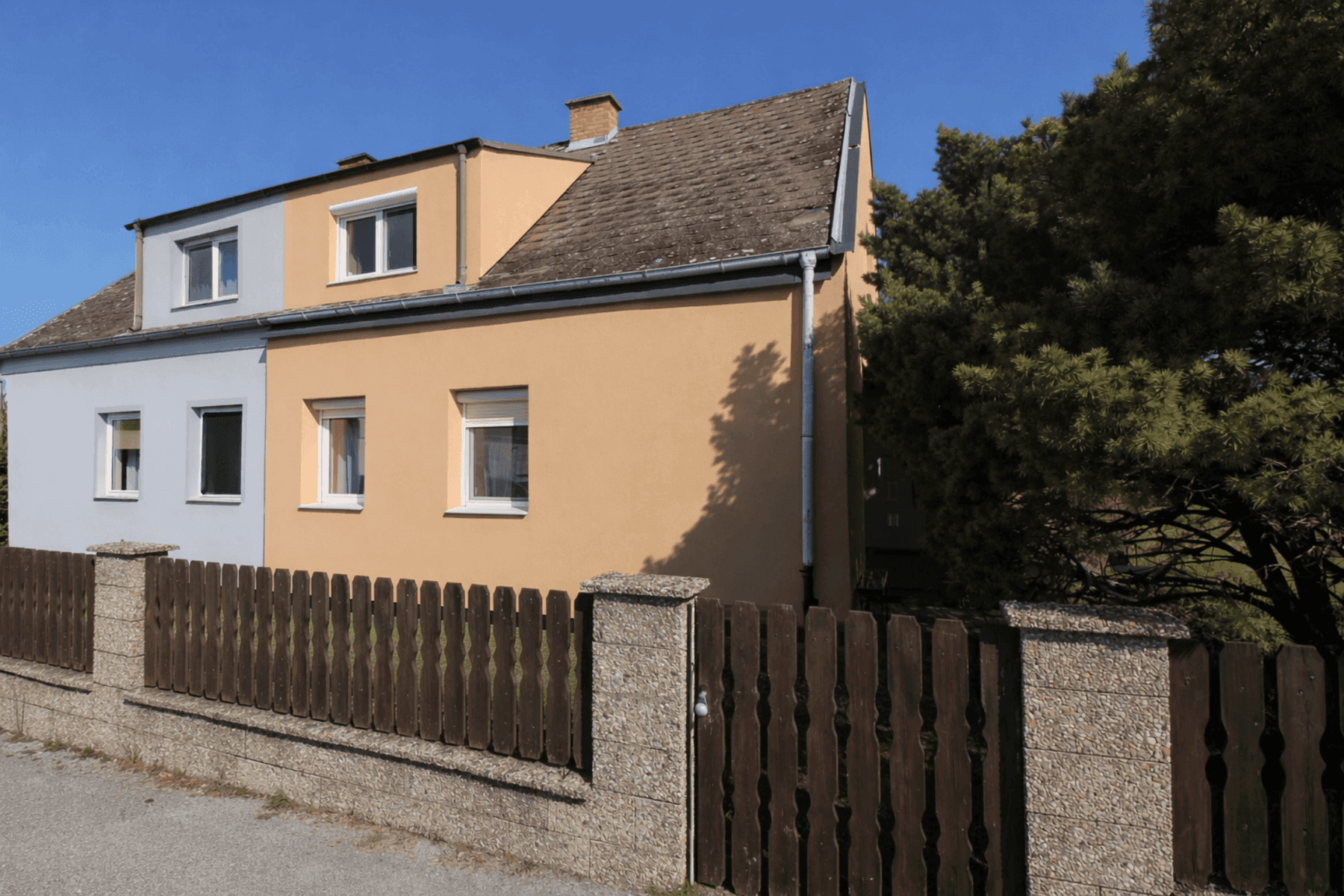 Fassade eines Einfamilienhauses mit mehreren Fenstern und einem Holzzaun im Vordergrund.