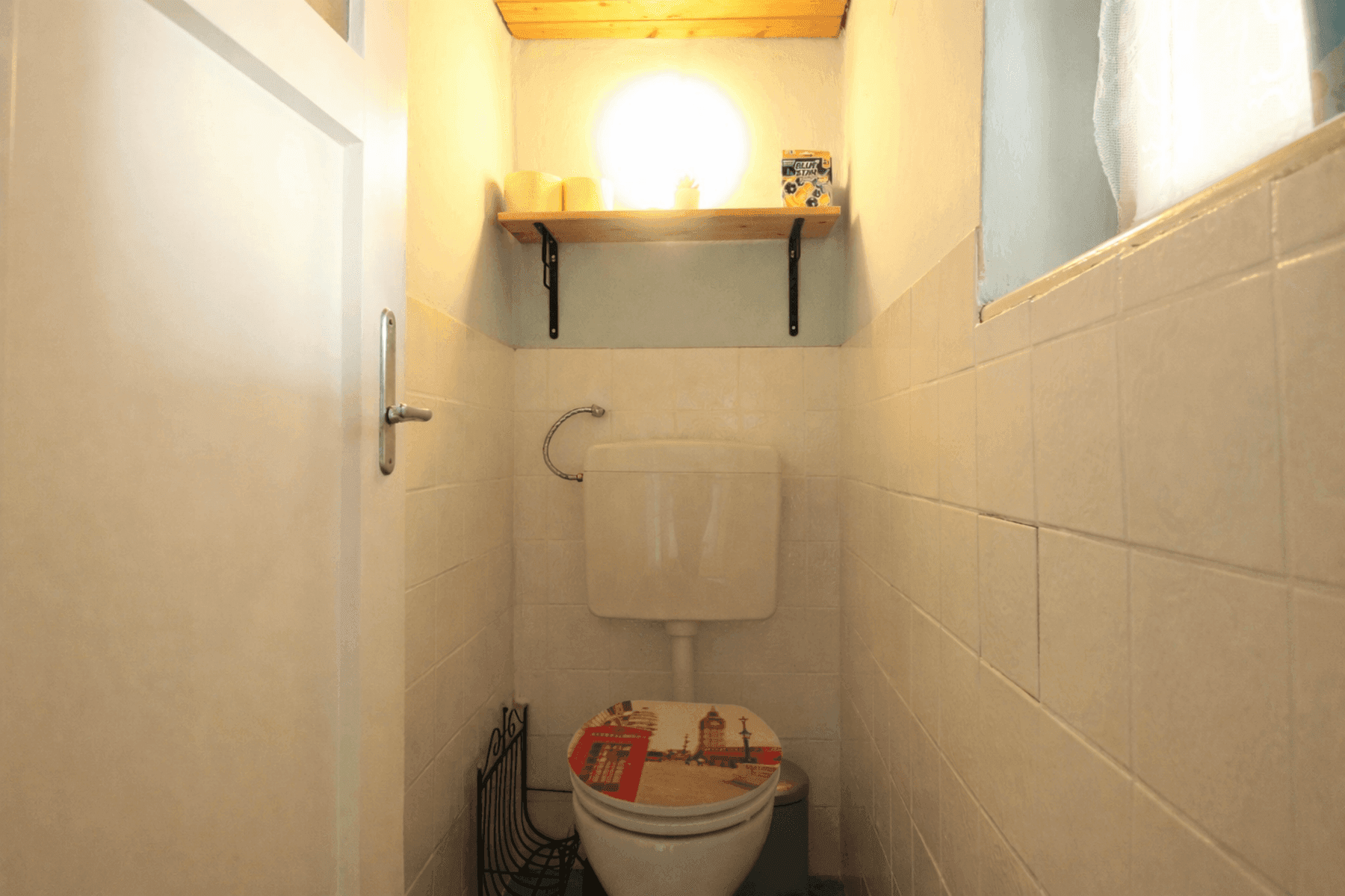 Kleines separates WC mit Fliesen an den Wänden und einem Fenster für Belüftung.