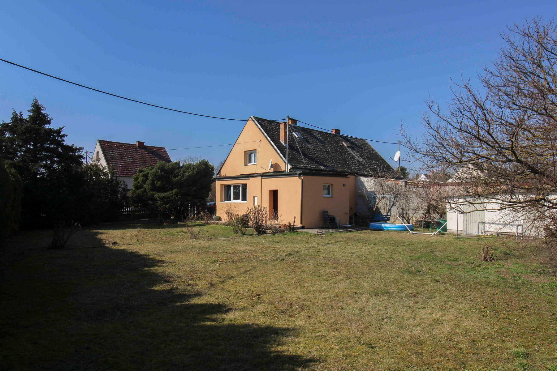 Großzügiger Gartenbereich mit Rasenfläche und einem Einfamilienhaus im Hintergrund unter blauem Himmel.