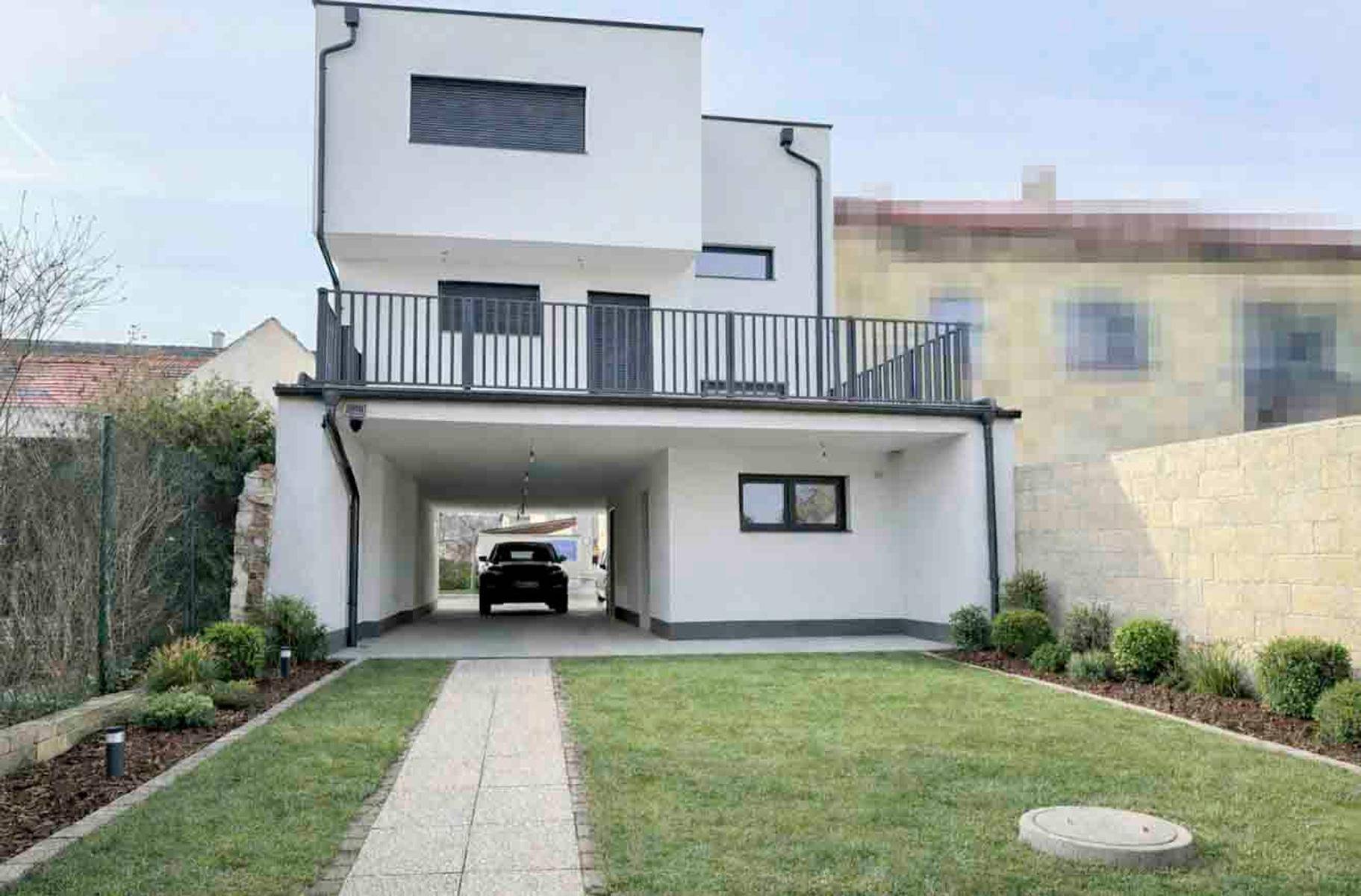 Modernes Wohngebäude mit Garten, Rasenfläche und überdachtem Stellplatz für ein Fahrzeug.