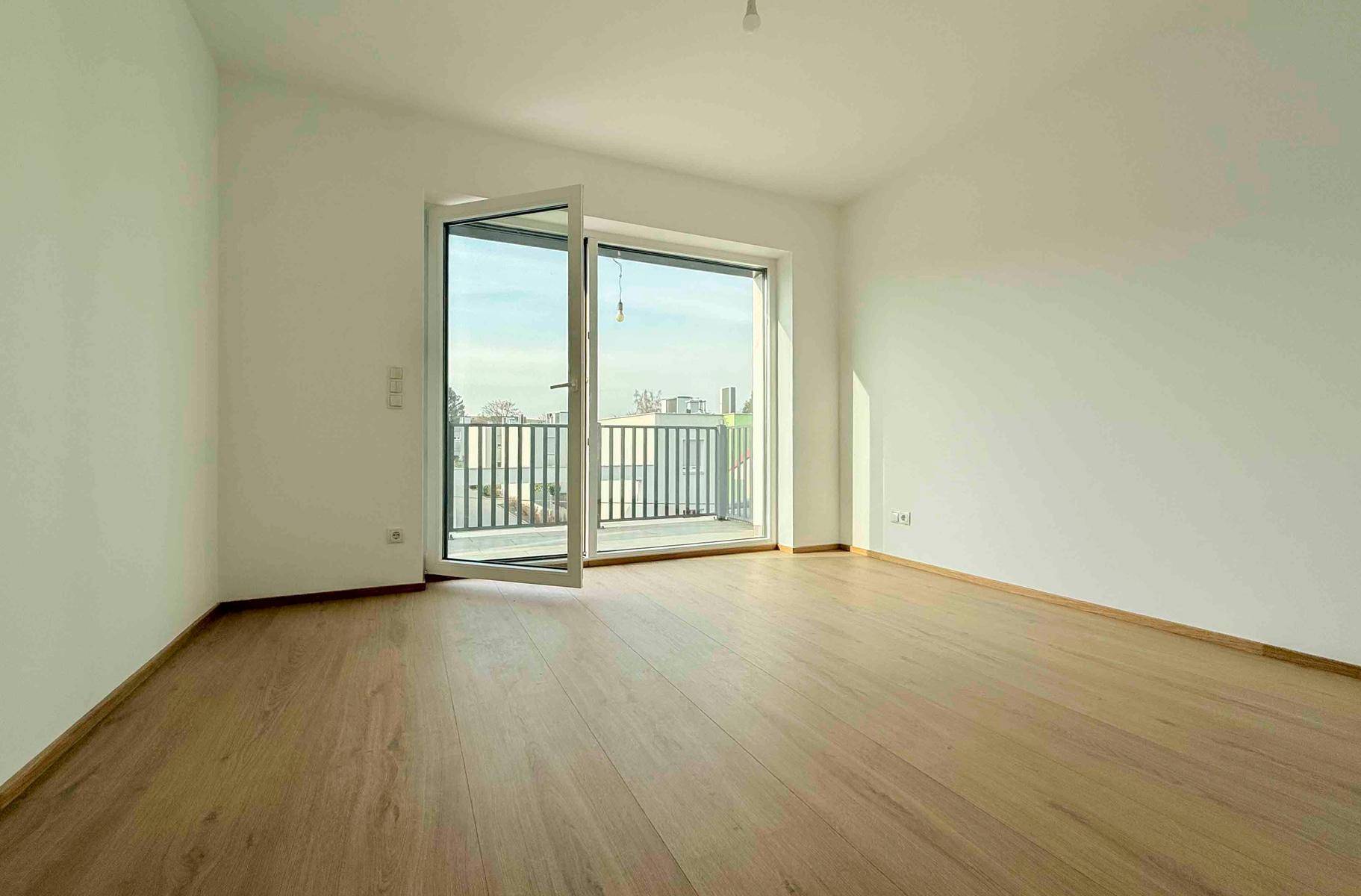 Heller, leerer Raum mit Laminatboden und Balkonzugang, ideal für ein Schlafzimmer oder Büro.