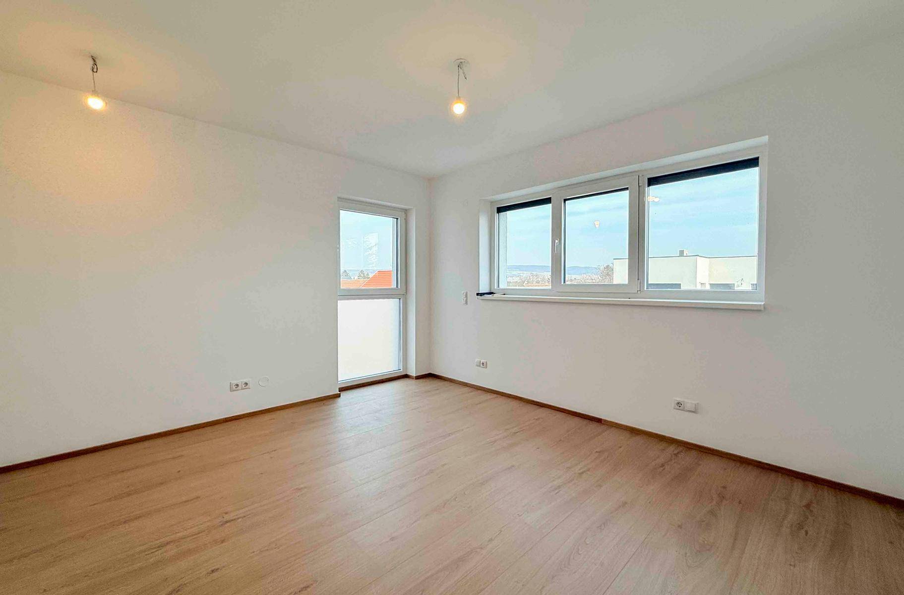 Heller, leerer Raum mit Laminatboden und großen Fenstern, ideal für individuelle Gestaltung.